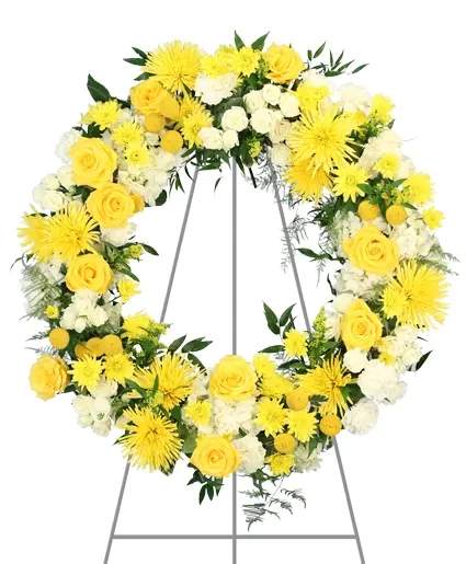 Glorious Glow Standing Wreath - Adorned in a beautiful display of white and yellow, Glorious Glow gracefully combines roses, carnations, and mums, evoking a serene tribute to cherished memories. Crafted with care and reverence, it offers hope and support during loss. We offer funeral home delivery to ensure this heartfelt expression reaches its destination.  Includes: Mache Wreath, Variegated Pittosporum, Plumosus, Italian Ruscus, White Carnations, Yellow Billy Buttons, White Hydrangeas, Yellow Cushion Poms, Yellow Roses, Yellow Solidago, Yellow Spider Mums, White Spray Rosesva.