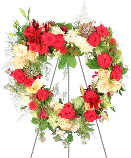 Heartfelt Compassion Standing Wreath - Embodying profound empathy, Heartfelt Compassion intertwines lush roses, lilies, and carnations in rich reds, pinks, and burgundy. Each bloom symbolizes heartfelt compassion, offering support during life’s difficult times. Order this arrangement today to offer enduring love and the eternal bond shared with the departed.  Includes: Open Heart Mache, Seeded Eucalyptus, Plumosus, Italian Ruscus, Salal, Succulents, Red Carnations, Green Hydrangeas, Burgundy Lilies, Red Roses, Safari Sunset, Raspberry Stock, Coral Roses, White Roses, Pink Hydrangeas.
