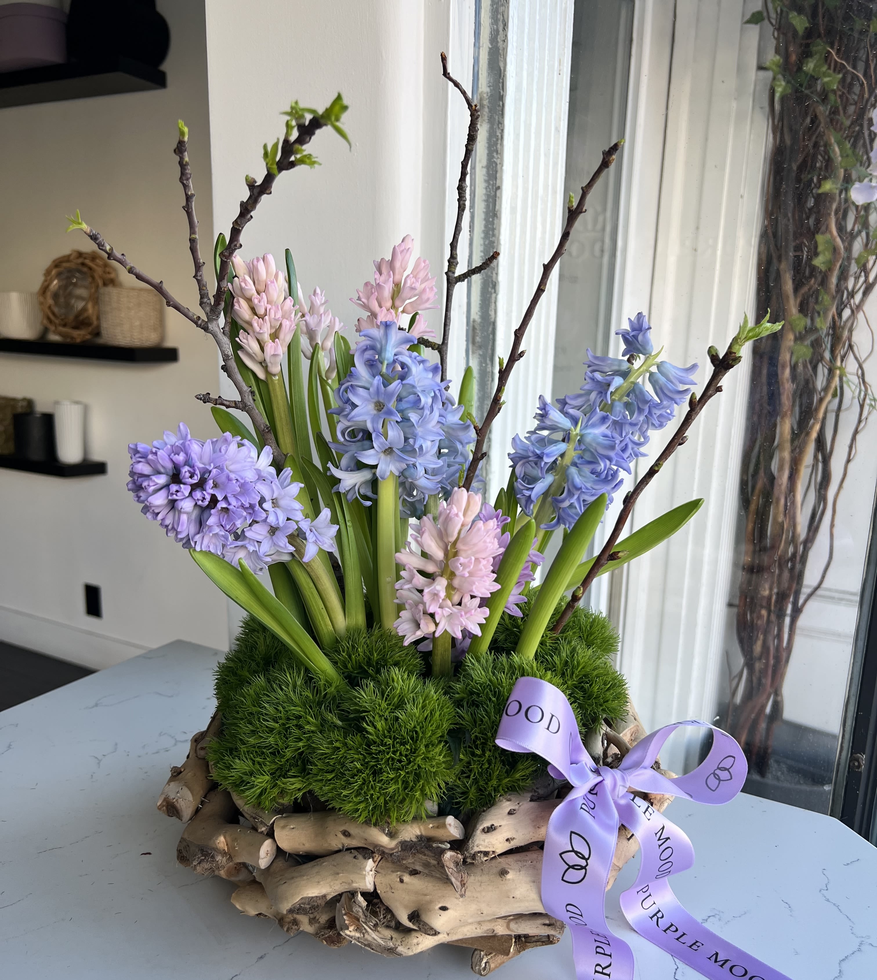 Arrangement of pastel hyacinths in a rustic wood base with a purple ribbon