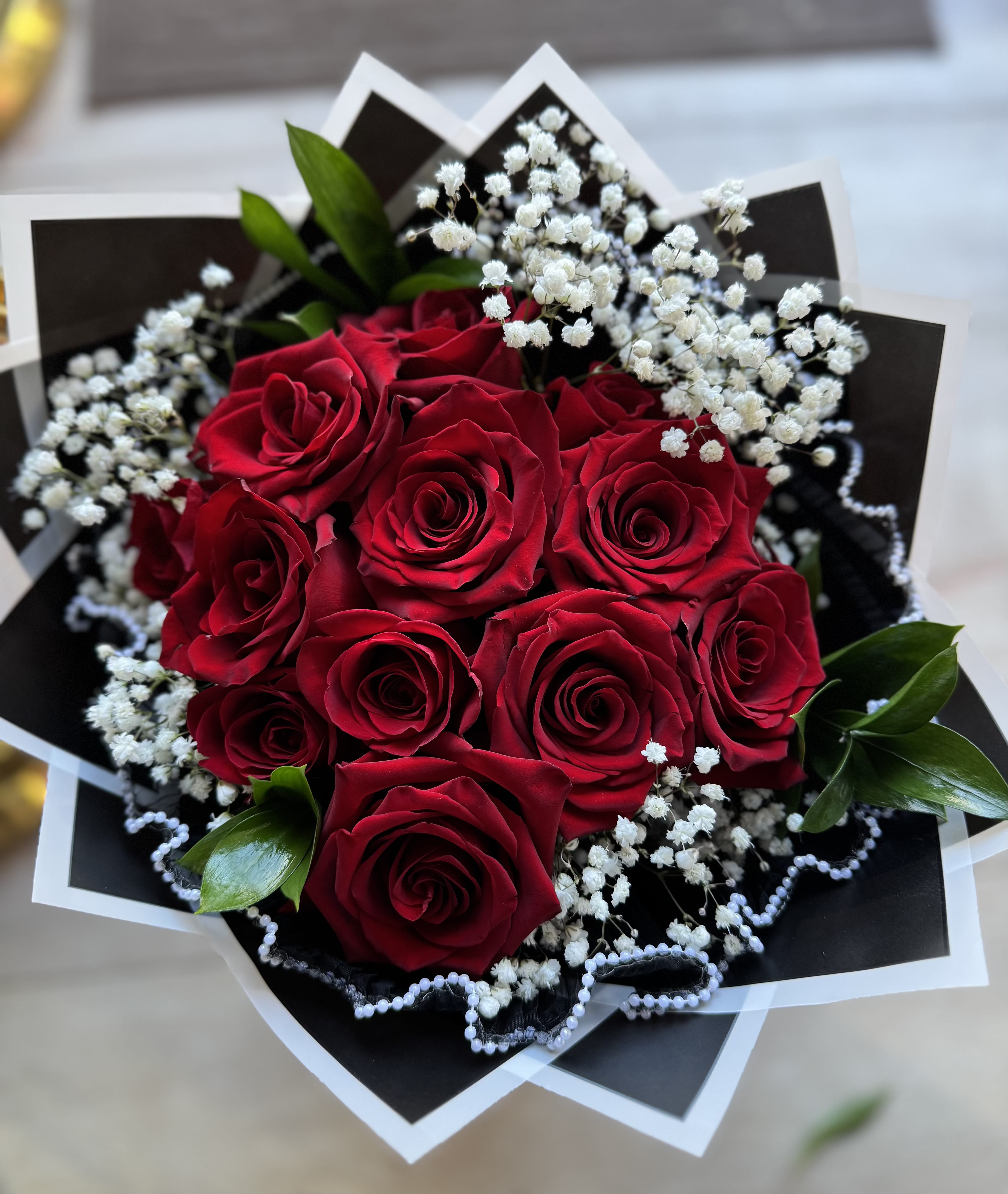 Red Roses Flower Bouquet - Make a grand statement with this breathtaking bouquet of premium long Steam red roses, beautifully accented with delicate sprigs of white baby's breath. Each velvety rose is carefully selected for its deep, rich color and flawless form, creating a lush, romantic arrangement. Wrapped in elegant black mesh with a striking geometric frame and pearl trim, this bouquet is the perfect blend of sophistication and passion. Ideal for anniversaries, proposals, or any special celebration where love takes center stage.  Standard 12 roses Deluxe 24 roses Premium 36 roses  Available to be added  -Pearl Mesh Wrapping  -Glass Vase  -Banner"message"  