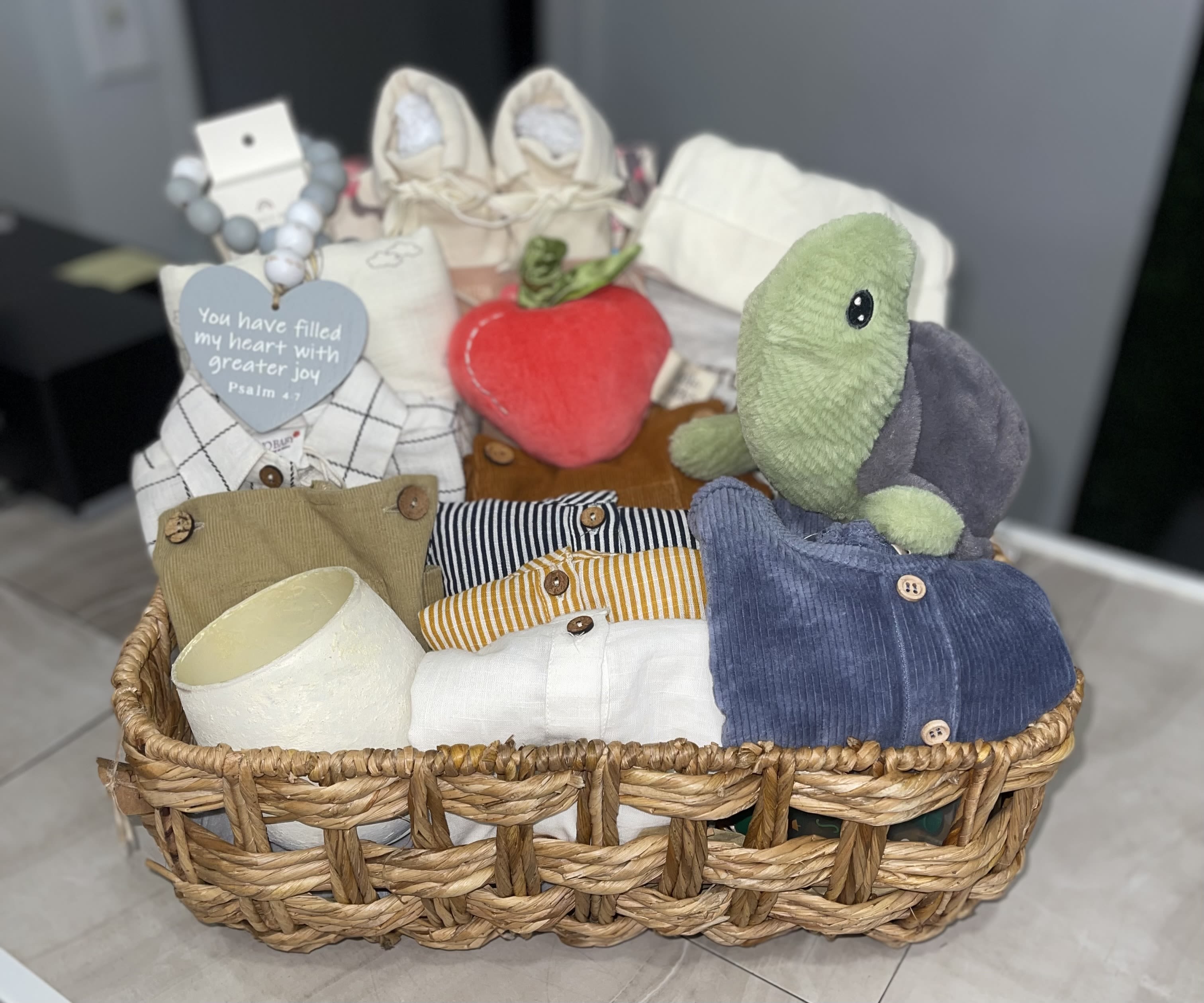 Large Hello Baby Boy Basket - Soft neutrals washed with navy, mint and pastel accents make this baby gift basket feel like a cozy nursery hug - perfect as a new baby or baby shower gift for a baby boy.  cuddly plush give the recipient a playful focal point, woven laundry-style basket presents everything neatly for a welcome‑home moment that says "we're so glad you're here."  Inside you'll find folded infant clothing in neutral, striped and blue tones, plus soft plush friends a green-and-gray turtle and a strawberry-shaped toy, all arranged on tissue paper. The mix of textures - wicker or white mesh basket, knit fabrics, folded baby clothes, a rolled blanket, heart-shaped tag, beaded bracelet and small gift packaging - creates a handmade, practical gift that's ready to display in the nursery. and a A variety of mixed blooms and foliage in a glass bud vase.  This basket is made to be given: thoughtful for new parents, sweet for a shower, and useful every day afterward. Choose the white mesh laundry-style option or woven basket presentation at checkout; items arrive gift-wrapped with a tag so the little one's first cuddles start the moment it's opened.