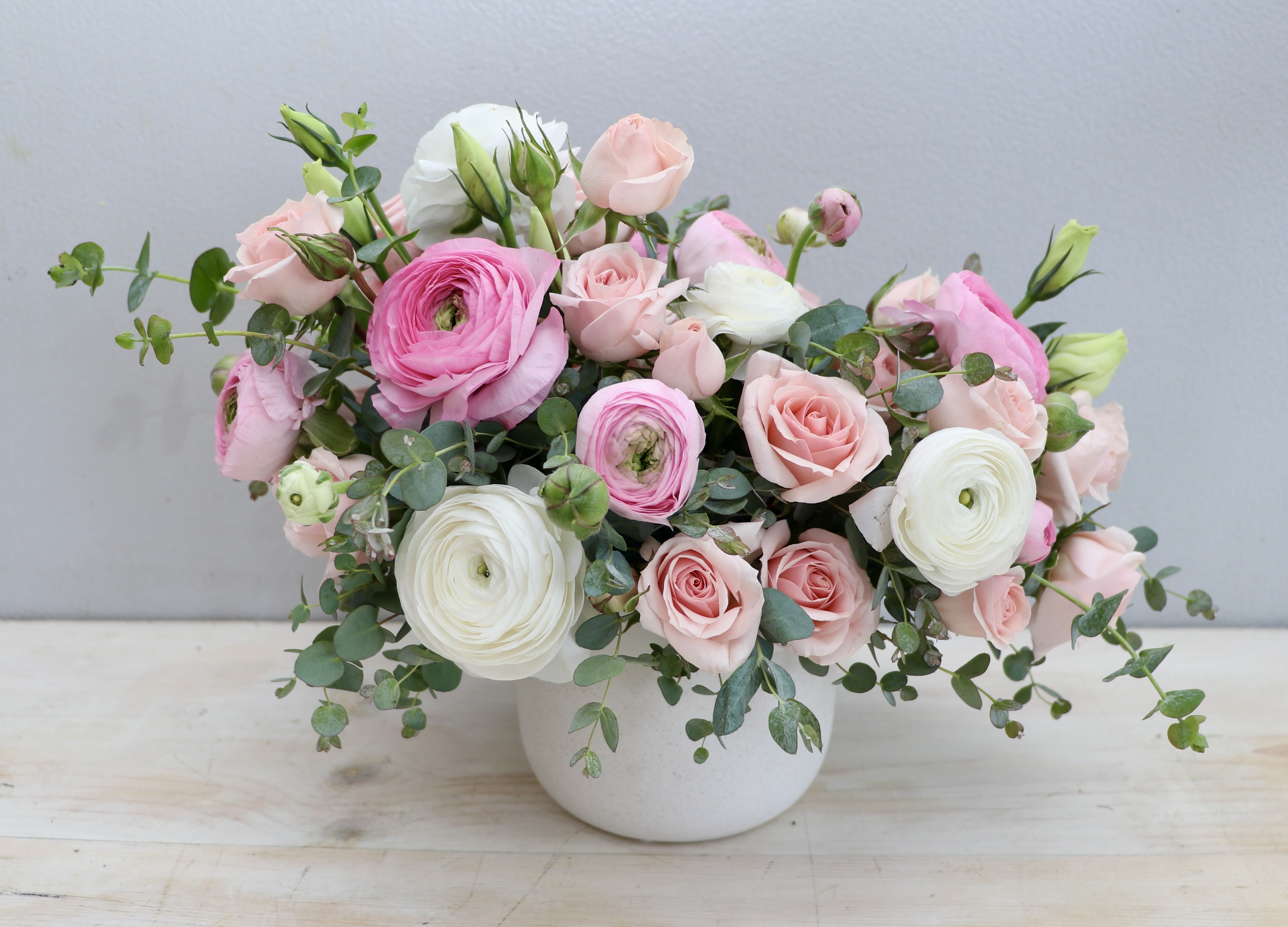 Low white pot filled with pink and white ranunculus and roses in a loose, rounded arrangement