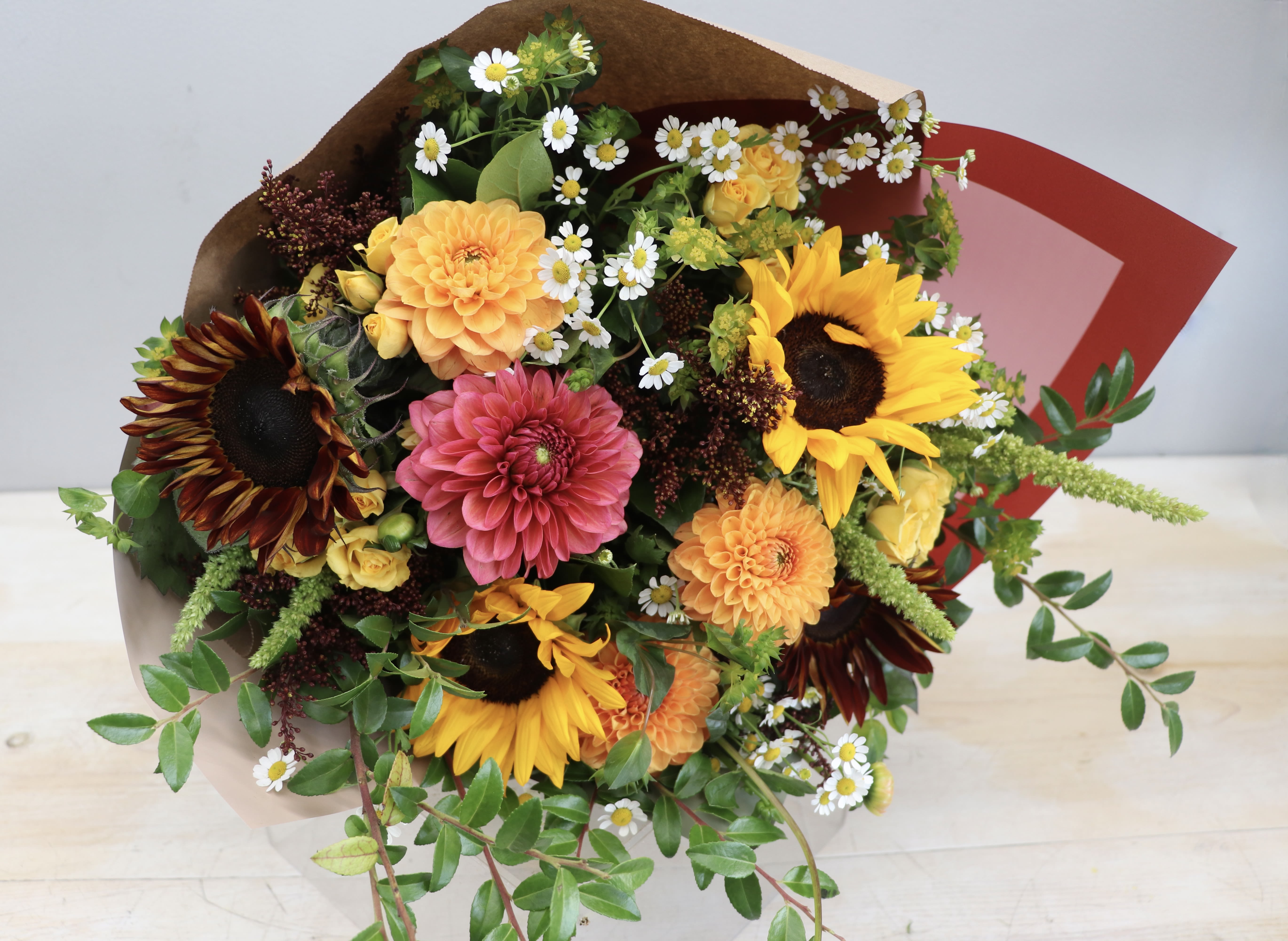 Bright bouquet with sunflowers, dahlias, spray roses, and small daisies wrapped in brown paper