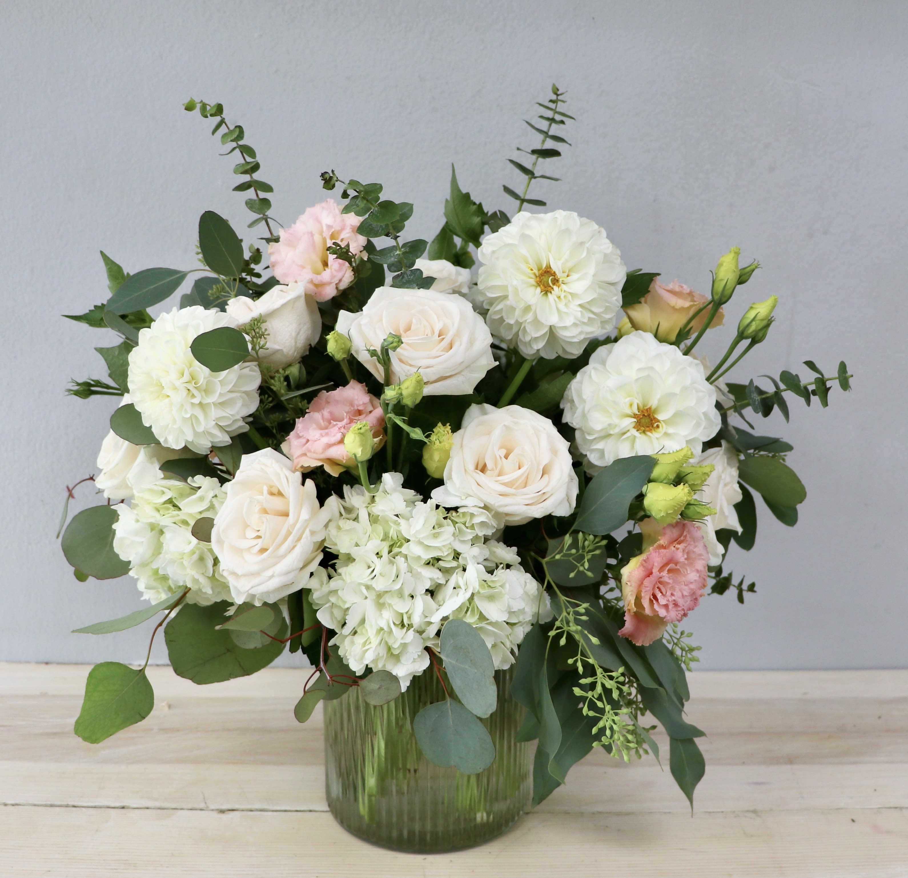 Dahlia &amp; Eucalyptus Meadow - Glendale Flowers - Artfully gathered in a textured glass vase, the design showcases a breathtaking mix of creamy white dahlias, soft blush-tipped lisianthus, and velvety garden roses. Nestled among pillowy white hydrangeas and framed by the whimsical movement of fresh eucalyptus branches, its airy, organic structure brings a touch of wild elegance to any space. Perfect for celebrating life’s special moments or simply bringing the romance of nature indoors.