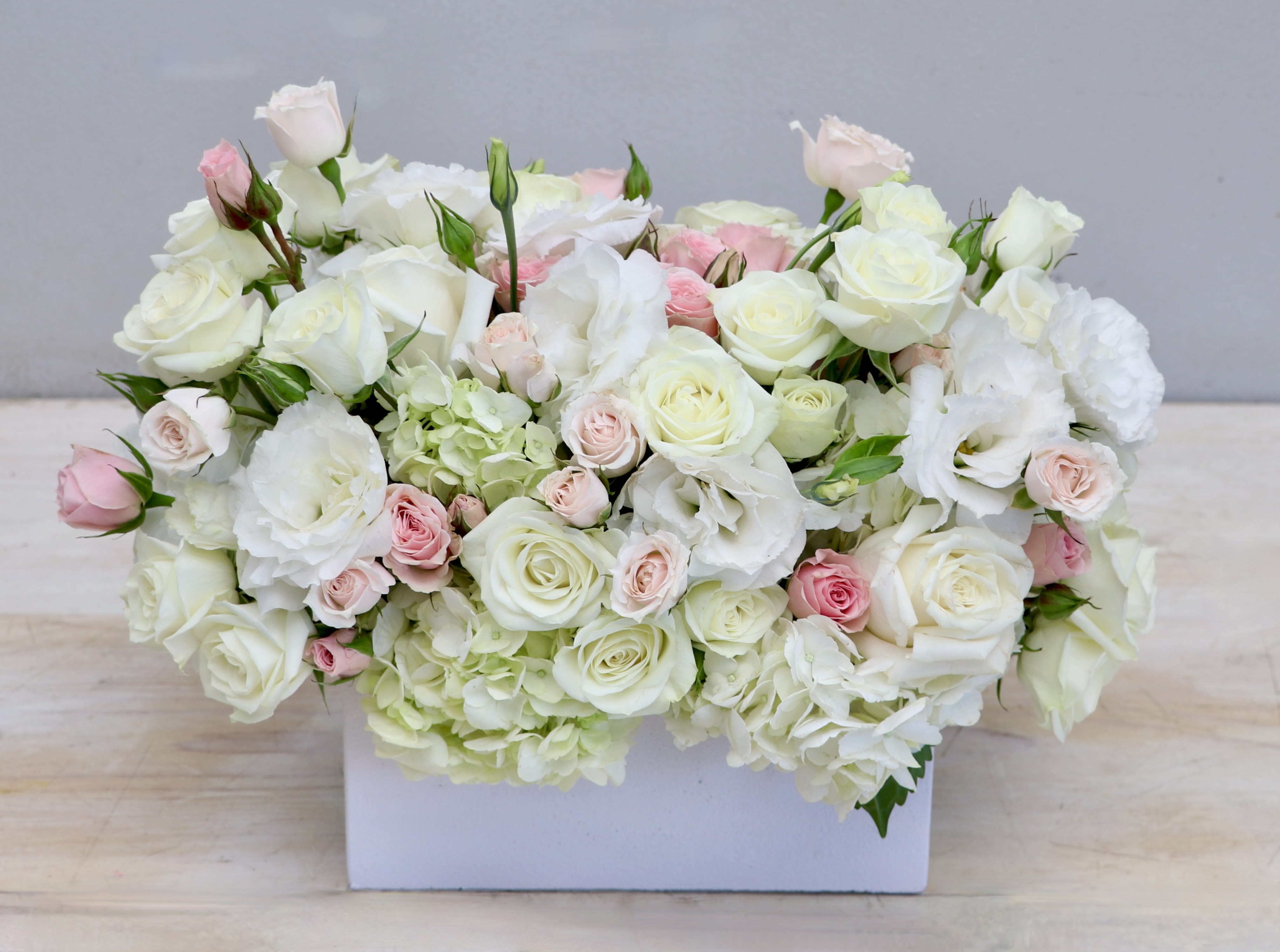 Low rectangular arrangement of white and pale pink roses and lisianthus in a white box.