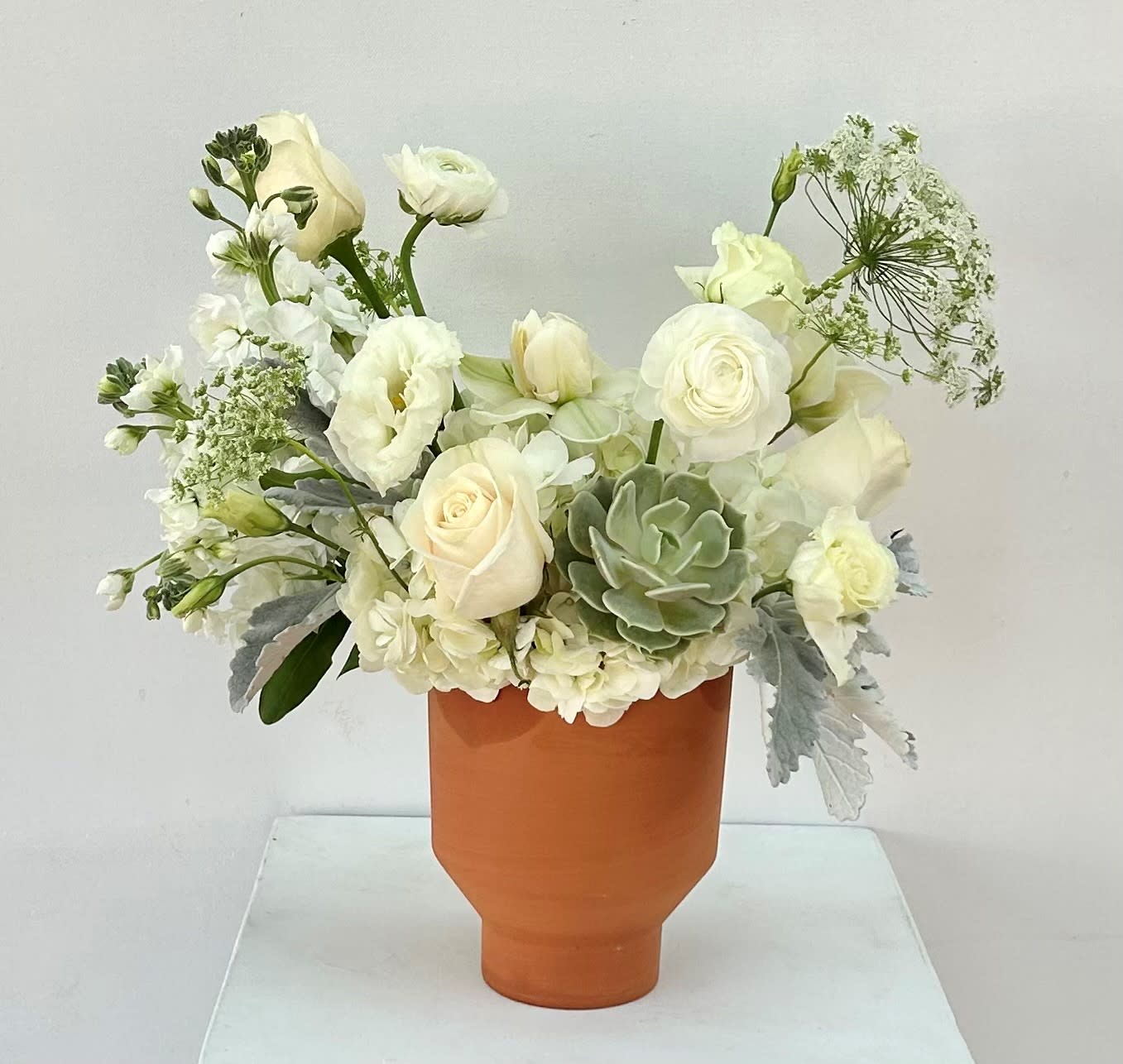 White floral arrangement in a terracotta vase with a green succulent
