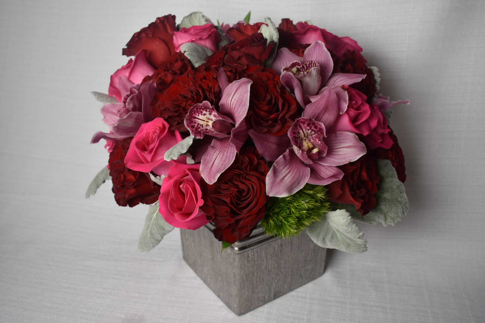 Red Pink Love - This beautiful arrangement comes in a square silver vase  with some Ecuadorian roses called heart with some touches of hot pink Ecuadorian roses combined with dusty miller and pink cymbidium orquids 