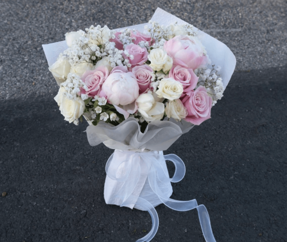Bouquet of pink and white roses with baby's breath, wrapped in white paper and ribbon