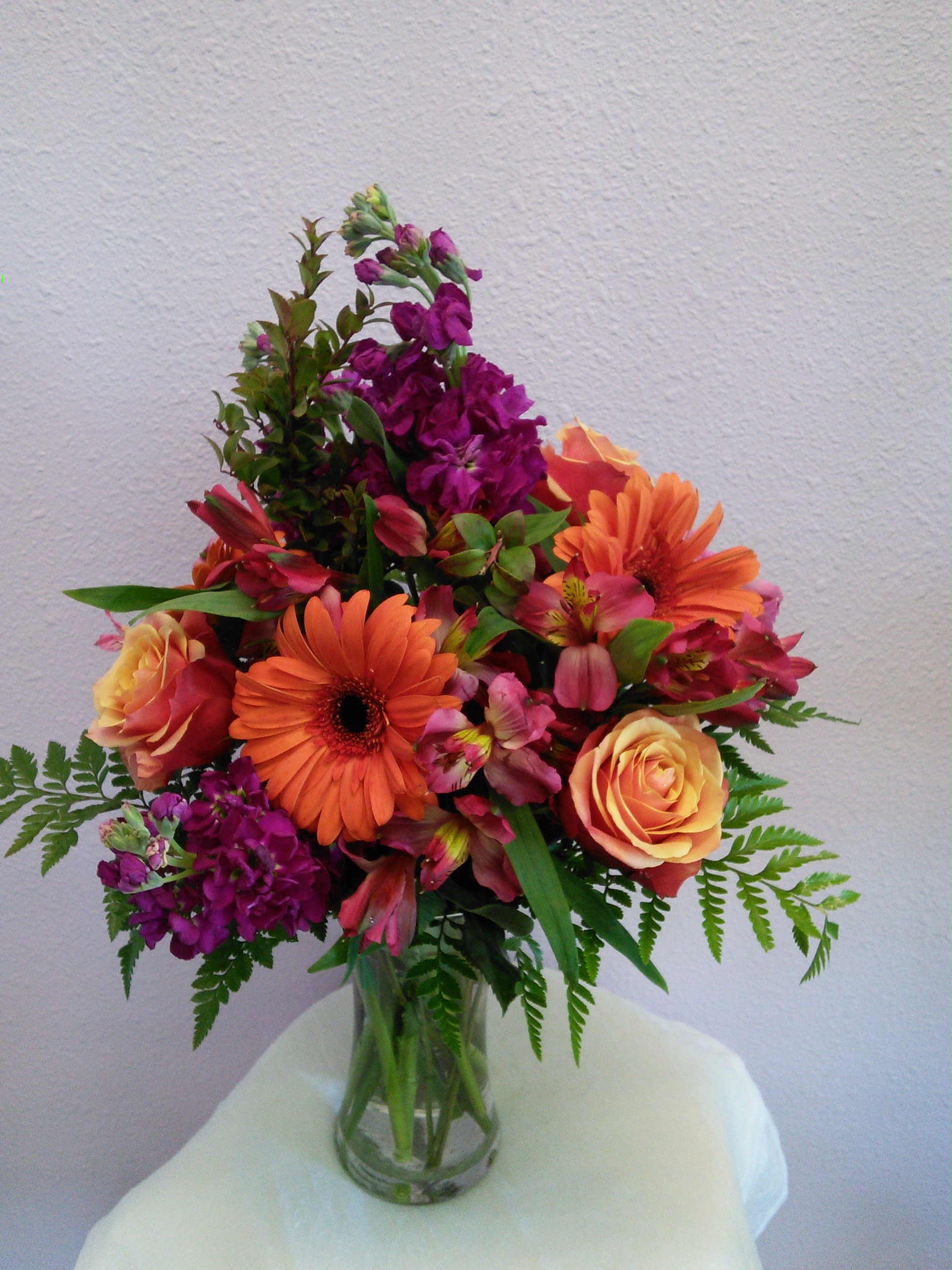Mixed bouquet of orange, pink, and purple flowers in a glass vase