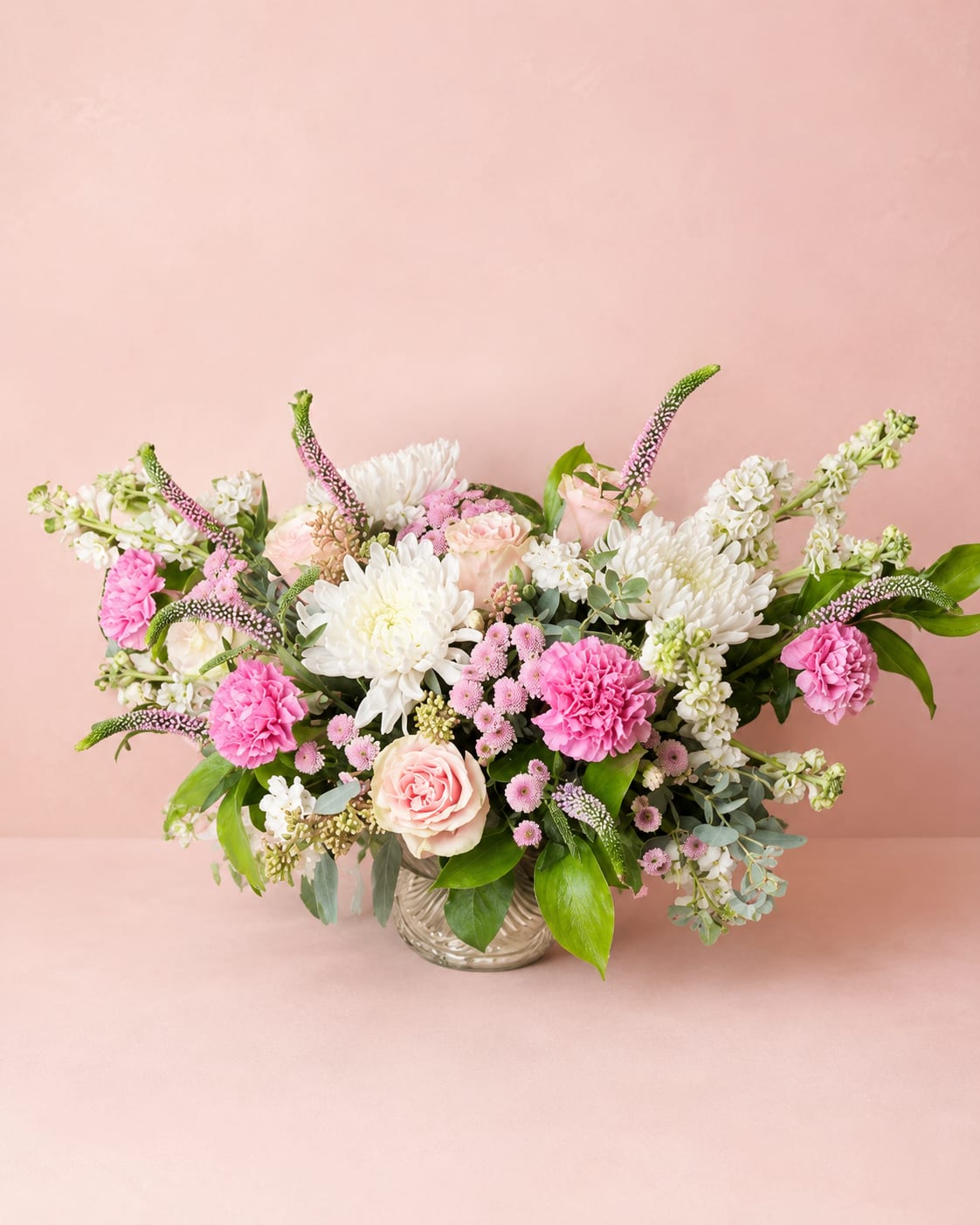 Eostre's Spring Awakening – Luxury Vase - Inspired by Eostre, the Germanic goddess of spring and new beginnings, this enchanting arrangement celebrates the beauty of the season's first blooms. Soft colors, graceful movement, and abundant textures create a design that feels fresh, joyful, and full of life.  Handcrafted in Flower Fairy's signature Butterfly Flight™ style, Eostre's Spring Awakening features premium roses, fragrant stock, chrysanthemums, carnations, veronica, button mums, eucalyptus, and other seasonal garden flowers. Its airy, wing-inspired silhouette and naturally flowing lines create a sense of movement, as if butterflies are drifting through a spring garden.  Perfect for birthdays, anniversaries, Mother's Day, congratulations, housewarmings, or simply celebrating life's beautiful moments.  Every arrangement is handcrafted by Flower Fairy using the freshest premium flowers available. Seasonal substitutions may occasionally be necessary while preserving the overall Butterfly Flight™ style, color palette, and value of the design.  Features: Flower Fairy signature Butterfly Flight™ design Premium seasonal flowers Roses, chrysanthemums, carnations, stock, veronica, and seasonal blooms Fresh eucalyptus and garden greenery Elegant glass vase Handcrafted by Flower Fairy Available in Standard, Deluxe, and Premium sizes Same-day flower delivery throughout the Phoenix Metro Area