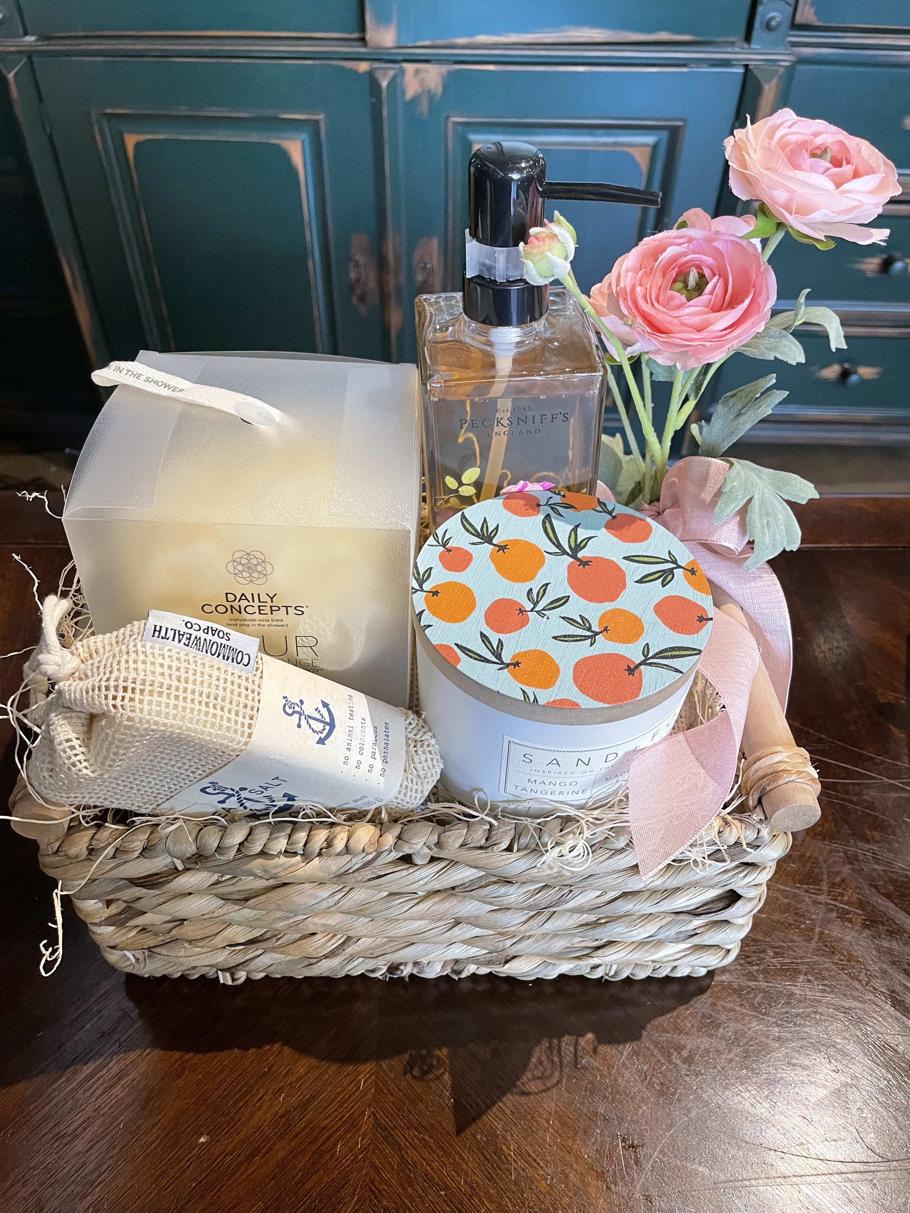 Gift basket with pink flowers, a soap dispenser, candle, and bath items