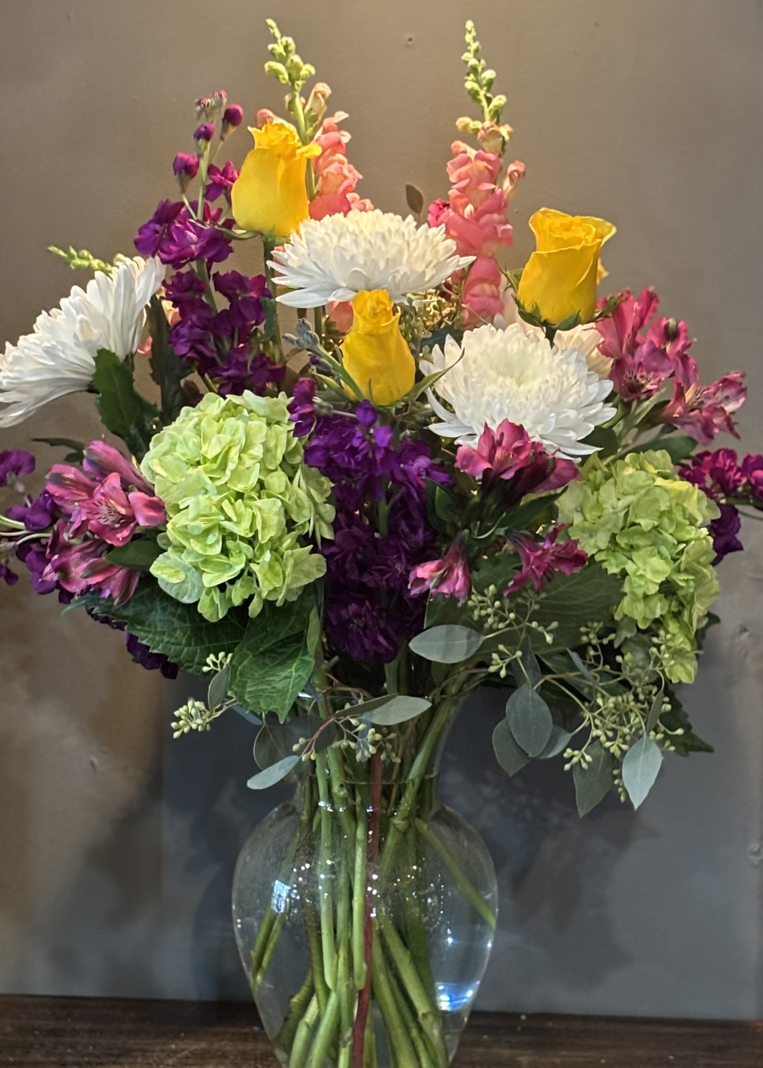 Mixed bouquet of yellow roses, white mums, and pink and green blooms in a clear glass vase