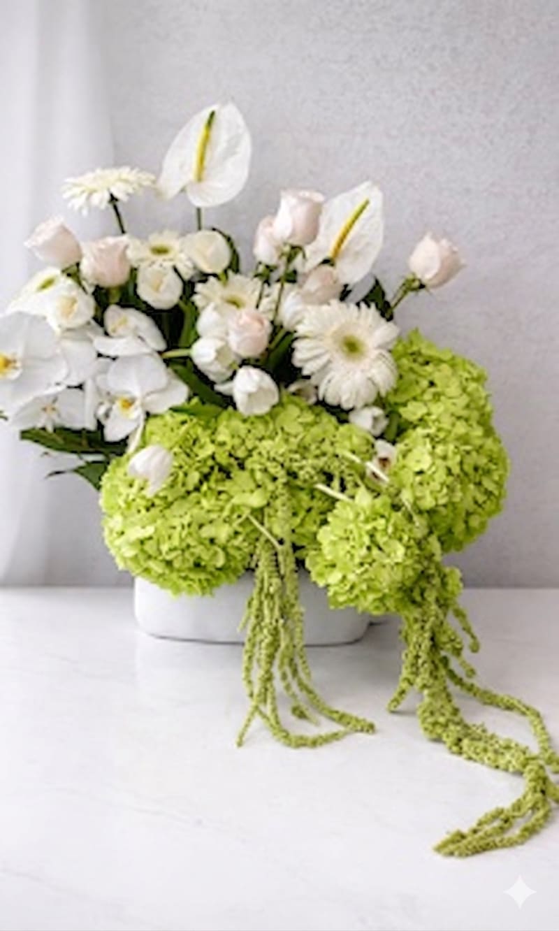 S&amp;M - Lime-green hydrangea clusters steal the show in this airy flower arrangement, a fresh and modern choice for a spring bouquet, housewarming gift, or thoughtful thank-you. The combination of green, white, and pale pink flowers creates a bright yet elegant impression-the kind of arrangement that makes the person you're thinking of feel noticed and uplifted.  This low white ceramic vase holds a rounded mass of hydrangeas accented with white roses, pale pink gerbera daisies, white orchid sprays, and tall white calla lilies that rise above for sculptural height. White daisy-like blooms add light texture and contrast against smooth calla stems; overall the palette reads clean and contemporary. Dimensions are suited for tabletops and entry consoles, giving a strong visual impact without overwhelming a room.  Ideal for welcoming someone into a new home, celebrating a spring moment, or saying thank you in a way that feels both refined and cheerful. The low ceramic vase makes placement easy-keep blooms in fresh water, trim stems slightly every few days, and display away from direct heat to extend their life.