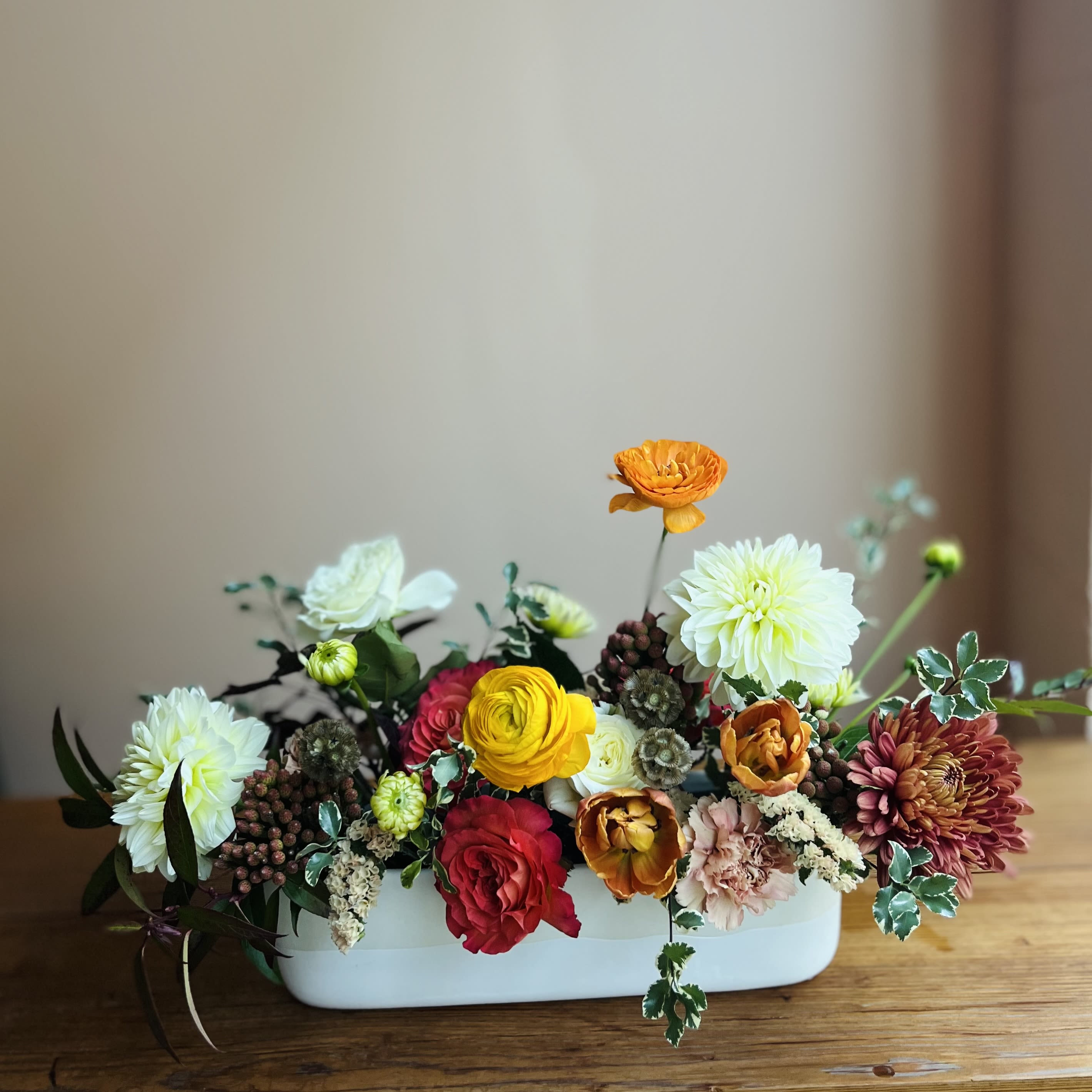 Mixed flower arrangement in a white rectangular vase with orange, red, yellow, and white blooms