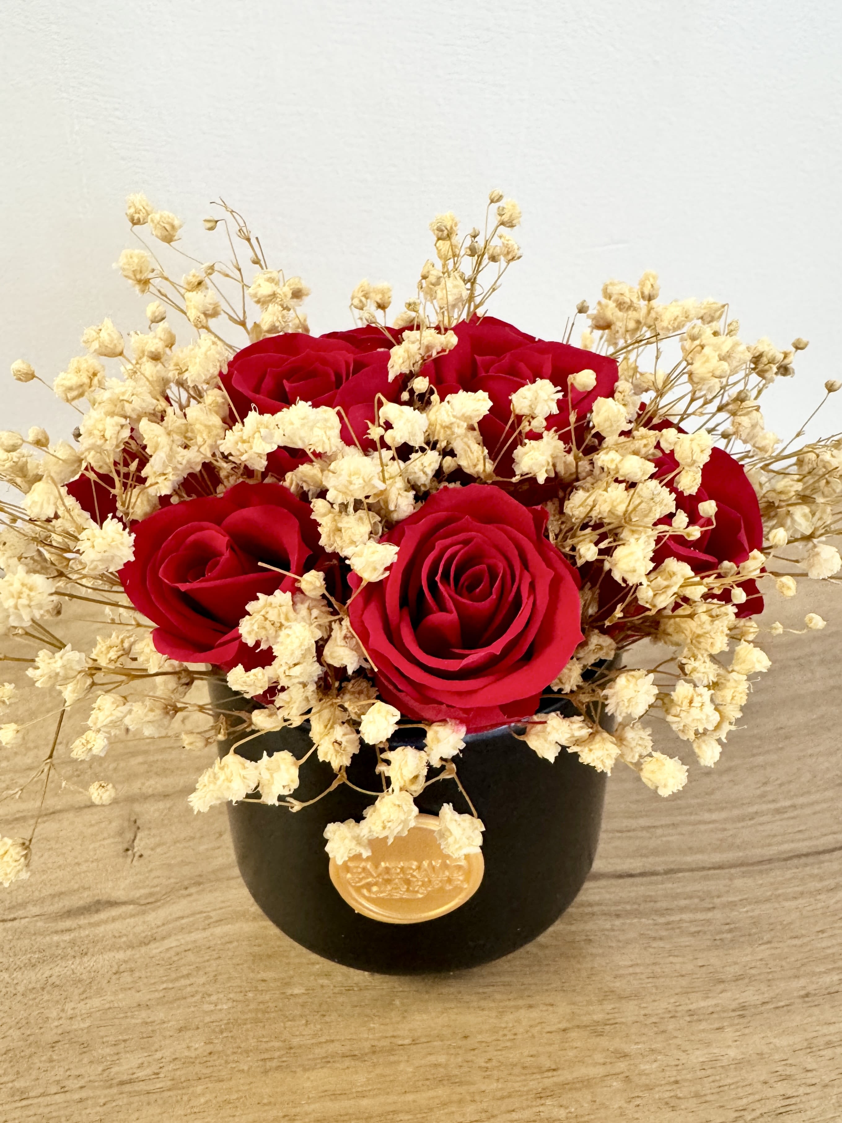 Éternelle Rouge Amour - Noir Mini - A timeless symbol of love and elegance, Eternelle Rouge Amour Mini features premium preserved red spray roses delicately accented with soft ivory baby’s breath, arranged in a sleek black vessel and finished with an elegant gold wax seal. Designed to last for years with no water or maintenance, this luxurious arrangement is perfect for anniversaries, birthdays, romantic occasions, or simply to brighten someone’s day.  Every Eternelle arrangement arrives beautifully presented in a premium gift box, making it the perfect choice for elevated gifting.  Care Tips: To preserve the beauty of your Eternelle arrangement, keep it in a cool, dry place away from direct sunlight, humidity, and heat sources. No watering or maintenance is required—simply enjoy its everlasting elegance. Avoid touching the roses frequently to maintain their delicate texture, and use a soft brush or gentle air duster to remove any dust from the petals or vase. With proper care, your arrangement will remain a stunning display of luxury for years to come.