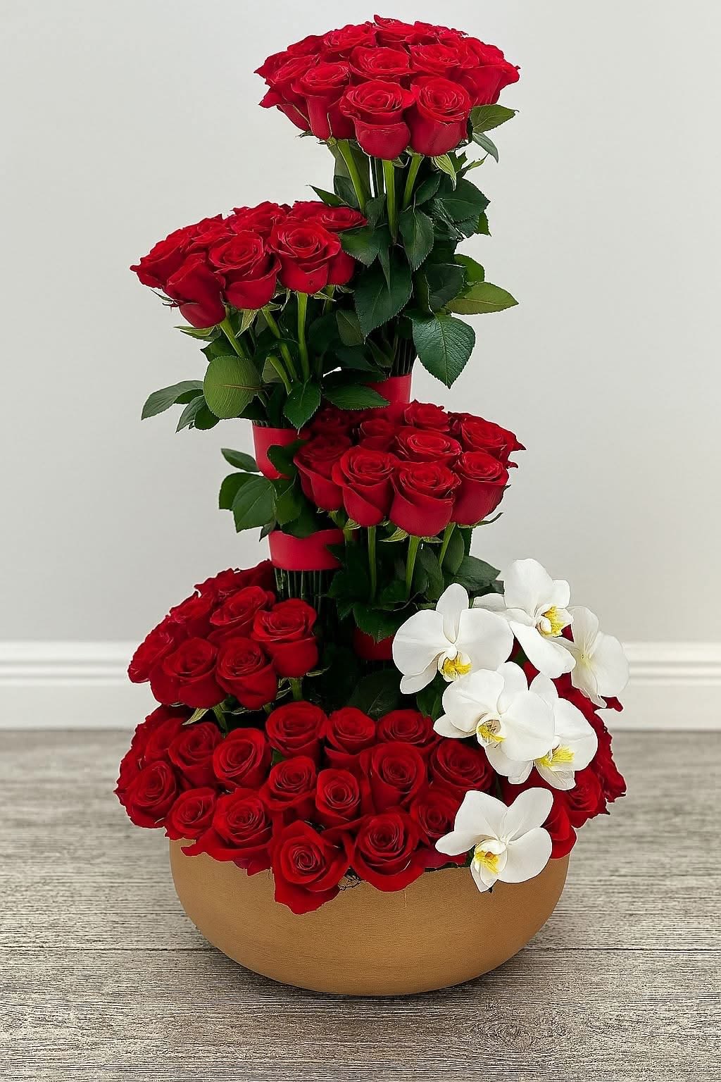 Royal Ascension - Royal Ascension is a breathtaking floral masterpiece designed for those who appreciate extraordinary luxury. Featuring approximately 100 premium red roses accented with elegant white Phalaenopsis orchids, this dramatic vertical arrangement is handcrafted to create a striking architectural silhouette that commands attention from every angle.  Created for life's most unforgettable celebrations, Royal Ascension is the perfect gift for milestone anniversaries, grand romantic gestures, luxury events, corporate spaces, or as an unforgettable statement of love and admiration.  Every arrangement is handcrafted by the floral designers at The Embassy of Flowers using only the finest premium blooms, delivering exceptional elegance, sophistication, and lasting beauty.  Includes: Approximately 100 premium red roses Premium white Phalaenopsis orchids Luxury designer vessel Professional floral design Complimentary personalized message card  Flower count may vary slightly depending on bloom size while preserving the artistic integrity and luxurious appearance of the design.
