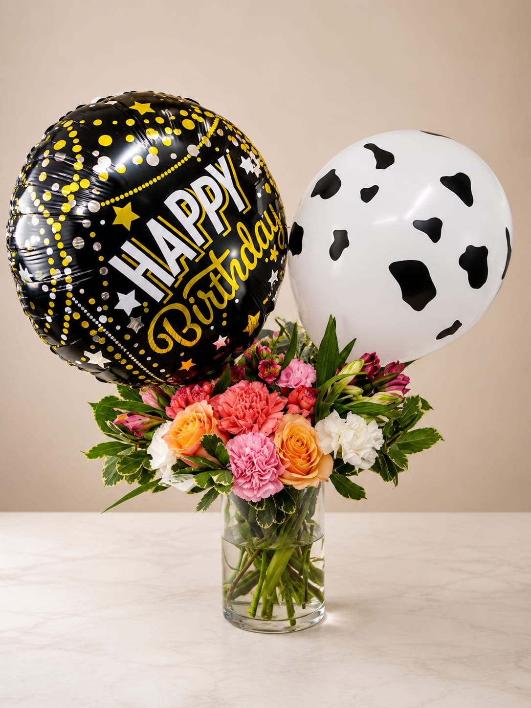 Brig - Bright, playful and perfect for a birthday surprise, this Brig flower arrangement pairs a compact mixed bouquet with two oversized balloons to make the recipient feel celebrated the moment the door opens. As a birthday arrangement it reads fun and festive-the black birthday balloon and the white cow-print balloon float above a cheerful cluster of roses, carnations and alstroemeria that say "happy day" in pinks, oranges and crisp white accents.  The bouquet sits in a clear glass vase so the stems and water are part of the clean, casual look. Roses bring soft, classic romance while carnations add ruffled texture and alstroemeria contributes delicate, freckled blooms for contrast-together forming a lively, mixed-color palette that photographs beautifully. The arrangement is compact and gift-ready, designed to fit on a table or countertop without overwhelming the space.  Ideal for friends, family members, coworkers, or anyone who enjoys a lighthearted celebration, this arrangement sends an unmistakable message of joy and thoughtfulness. Balloons are secured above the vase for delivery-ready presentation; to keep the flowers fresh, replace vase water every two days and trim stems slightly if needed.