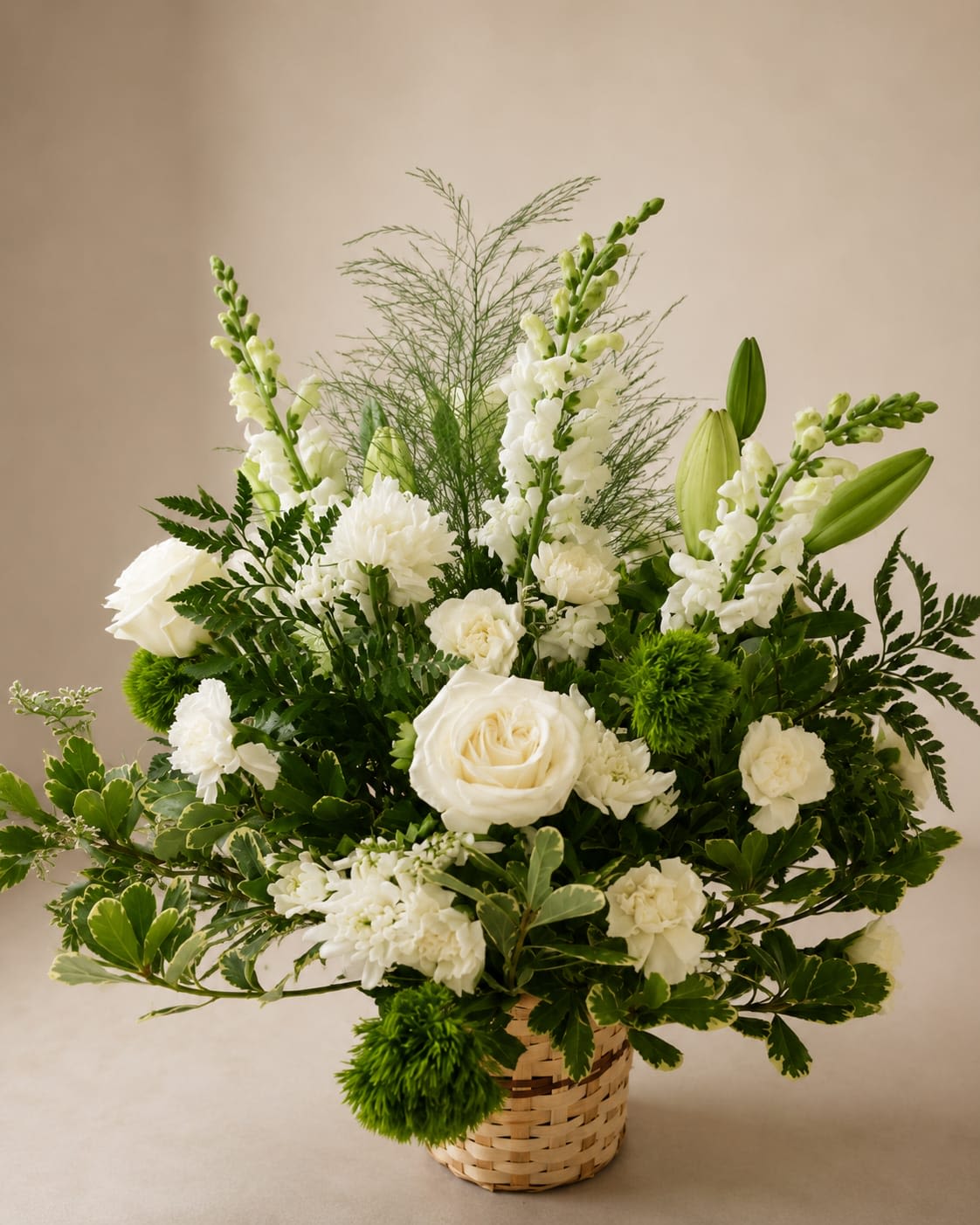 Pure Serenity - Pure white roses, lilies, carnations and tall snapdragons rise from a woven basket to create an elegant sympathy arrangement or refined wedding centerpiece. The upright, structured silhouette and serene white-and-green palette make this flower arrangement ideal for moments that call for quiet beauty-the person receiving it will feel thoughtfully remembered and comforted.  This arrangement combines white roses, carnations, lilies, snapdragons and chrysanthemums with bright green accent blooms and varied foliage for crisp contrast and texture. The composition is full and upright, with taller spikes at the back and broader movement at the base, presented in a natural woven basket that adds organic warmth and stability.  Perfect for funerals, memorial services, weddings, or as a peaceful gift to send your condolences or congratulations, Pure Serenity arrives ready to display. The basket keeps the design contained and easy to place; no special care beyond fresh water and a cool spot is needed to keep blooms looking calm and collected.