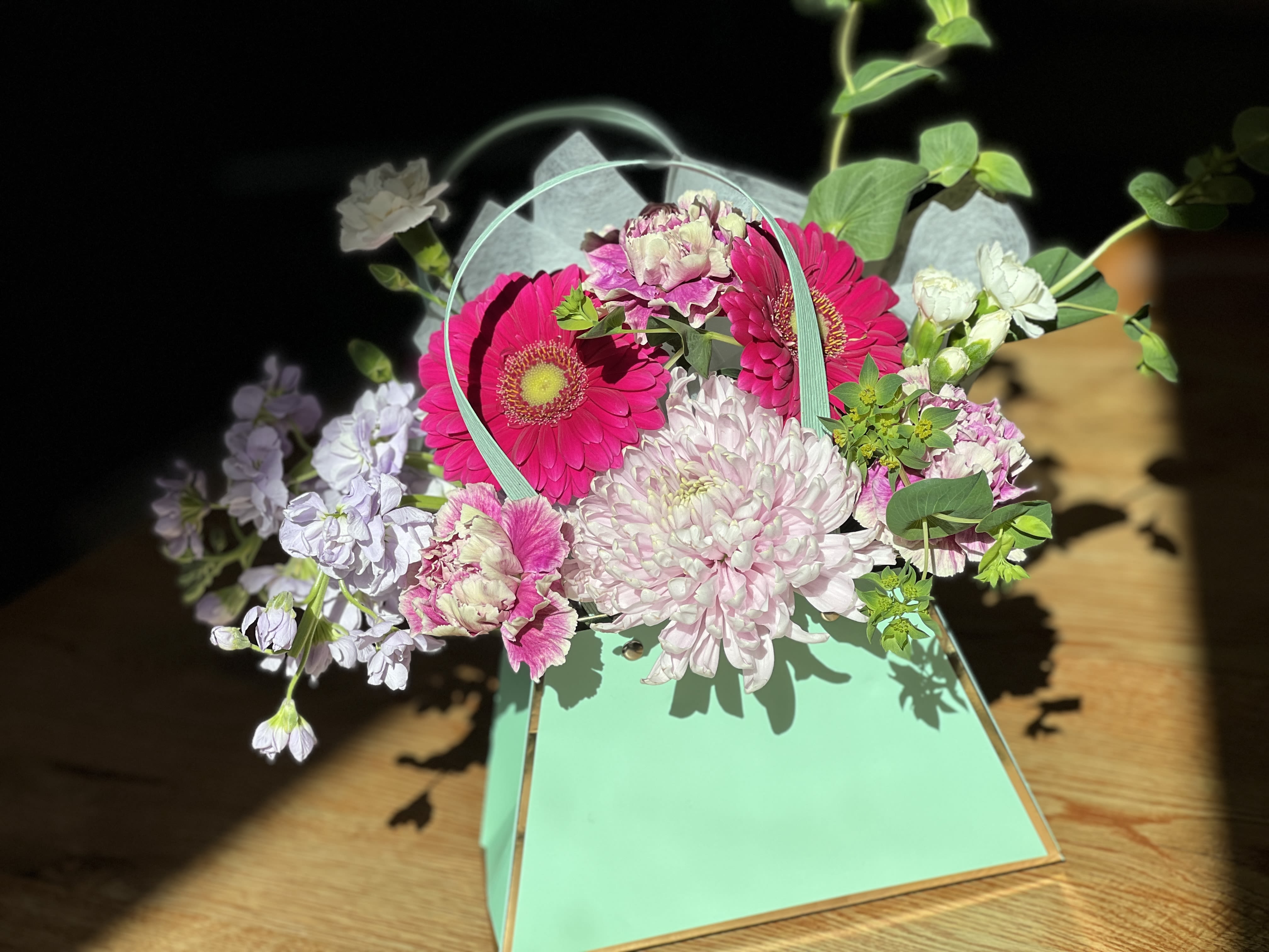 Pink and white flowers arranged in a mint green handled box