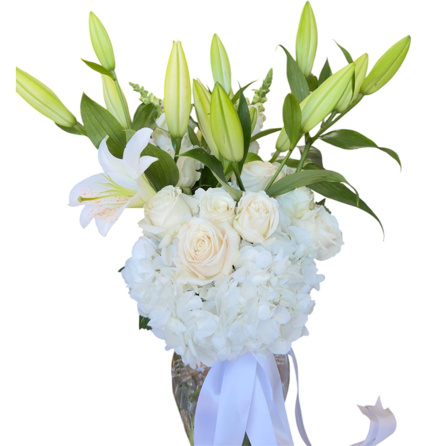 White  Serenity - Crisp white lilies and cream-toned roses create a serene statement bouquet perfect for a wedding centerpiece or a sympathy arrangement that offers quiet comfort. The tall, layered silhouette-unopened lily buds rising above a rounded mass of white hydrangeas-gives the recipient a feeling of calm and thoughtful presence, the kind that says "I'm here for you" without words.  Arranged in a clear glass vase with a soft white ribbon, this floral design emphasizes texture and purity: velvety rose petals, the sculpted petals of lilies, and the cloudlike fullness of hydrangea clusters in a harmonious white-and-green palette. The vase provides a clean, modern presentation that suits both formal and intimate settings.  Ideal for ceremonies, memorials, or to mark a quiet milestone, this arrangement arrives ready to display; keep blooms in fresh water and out of direct heat to extend their life. Its classic colors and elegant profile make it a thoughtful gift for someone you want to comfort or celebrate with understated grace.
