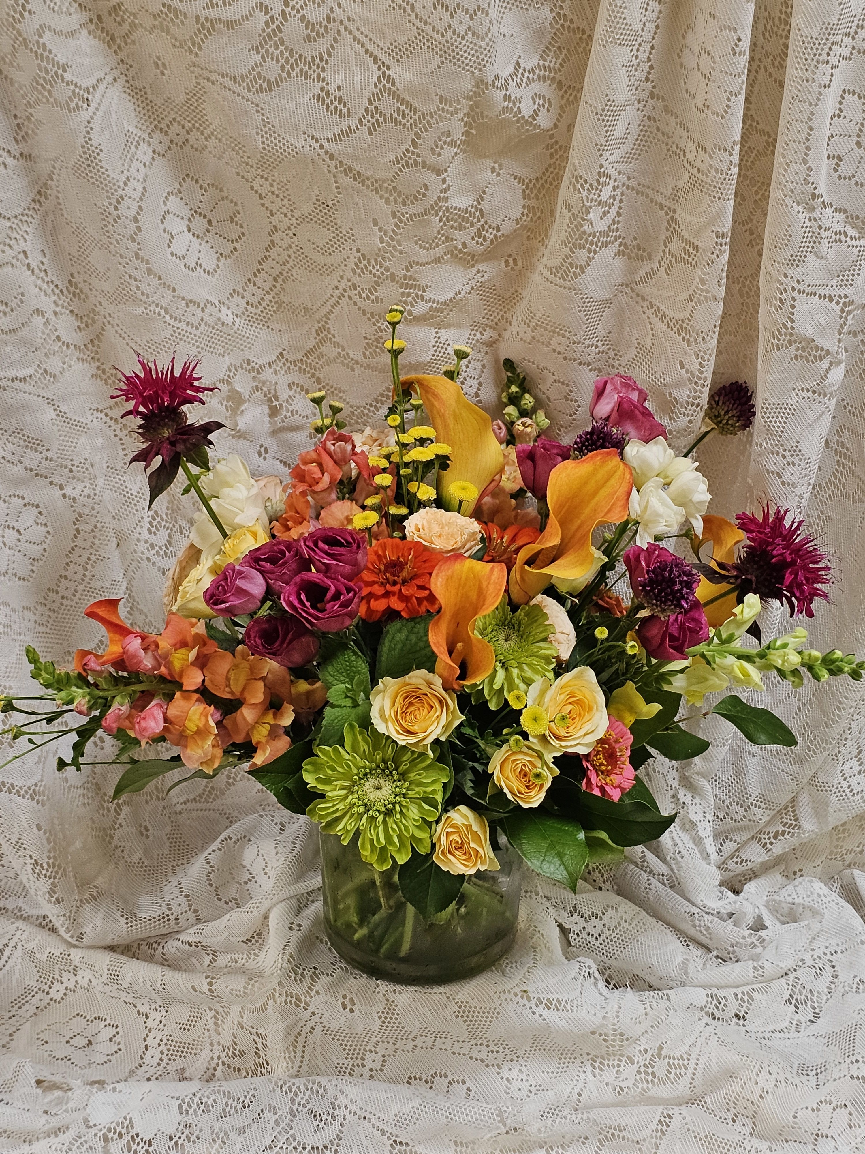 Sherbert Smiles - Bright, cheerful, and bursting with sunshine, Sherbet Smiles is a vibrant floral arrangement inspired by the refreshing colors of your favorite summertime sherbet. Designed in a low clear glass vase, this lush, garden-style arrangement overflows with hot pinks, juicy oranges, sunny yellows, and soft pink blooms, creating a joyful blend that's as sweet and colorful as a scoop of frozen summer.