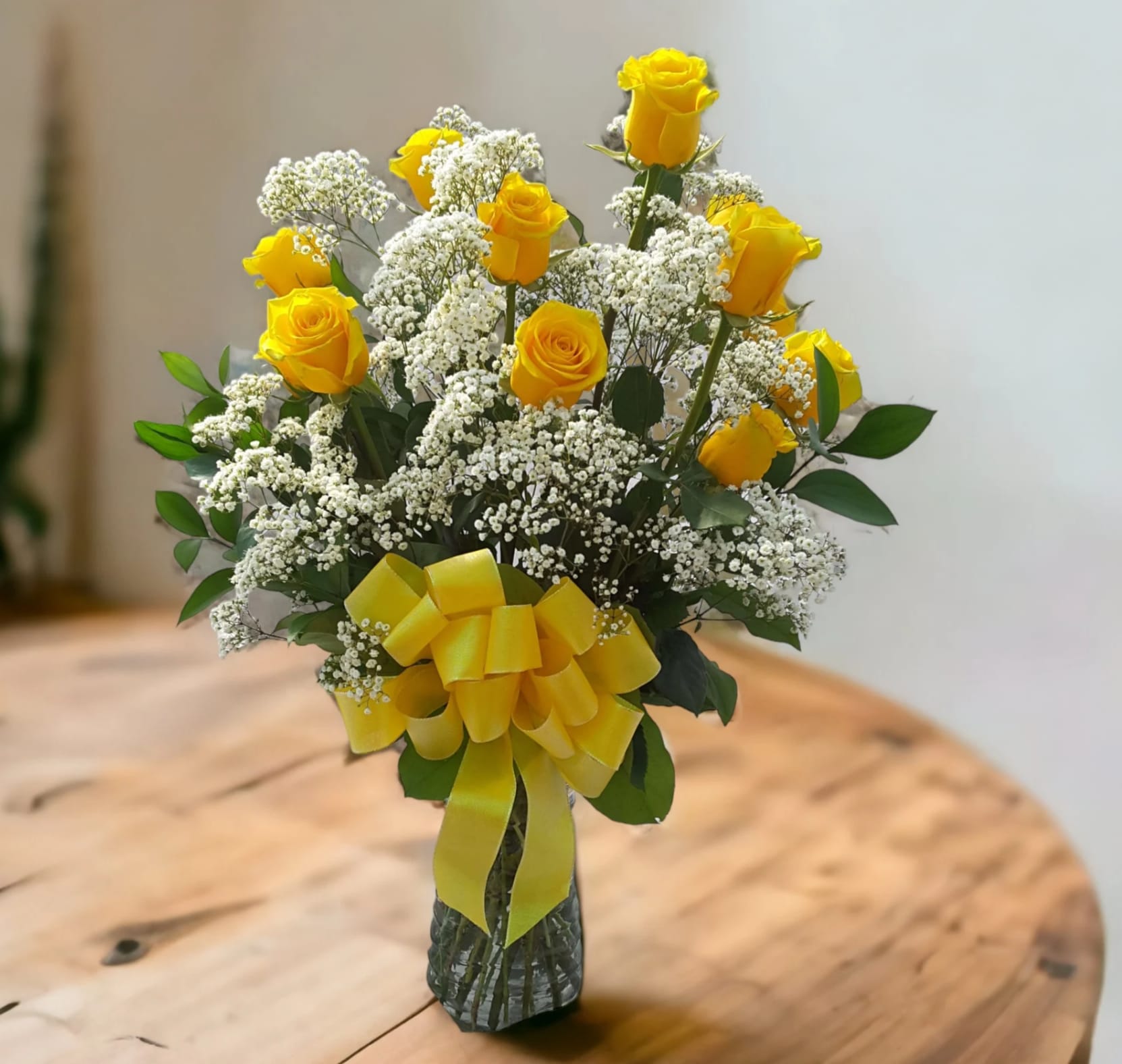 Yellow roses with white baby's breath in a glass vase tied with a yellow ribbon.