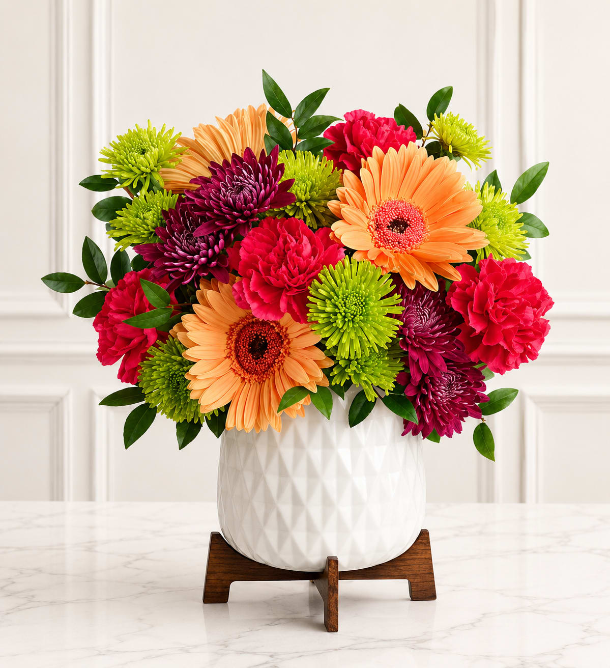 Peach Blossom Delight™ - Brighten any occasion with the cheerful beauty of the Peach Blossom Delight™. This fresh floral arrangement features elegant peach gerbera daisies, vibrant hot pink carnations, deep burgundy cushion mums, green button mums, and lush seasonal greenery, beautifully arranged in a modern white ceramic planter. Bursting with color and texture, this charming design is perfect for birthdays, thank-you gifts, celebrations, or simply letting someone know you're thinking of them.