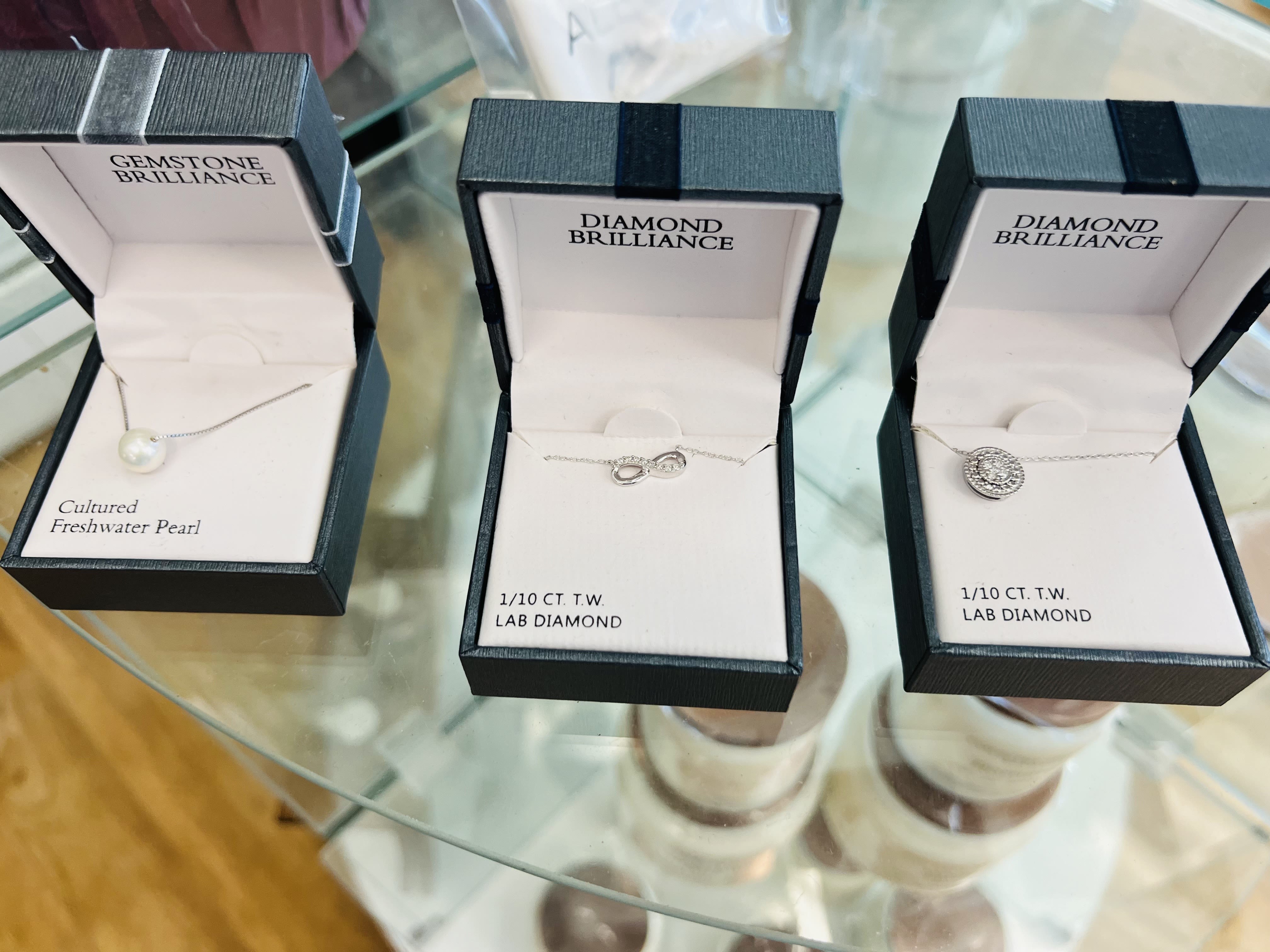 Three open jewelry boxes with necklaces on a glass table
