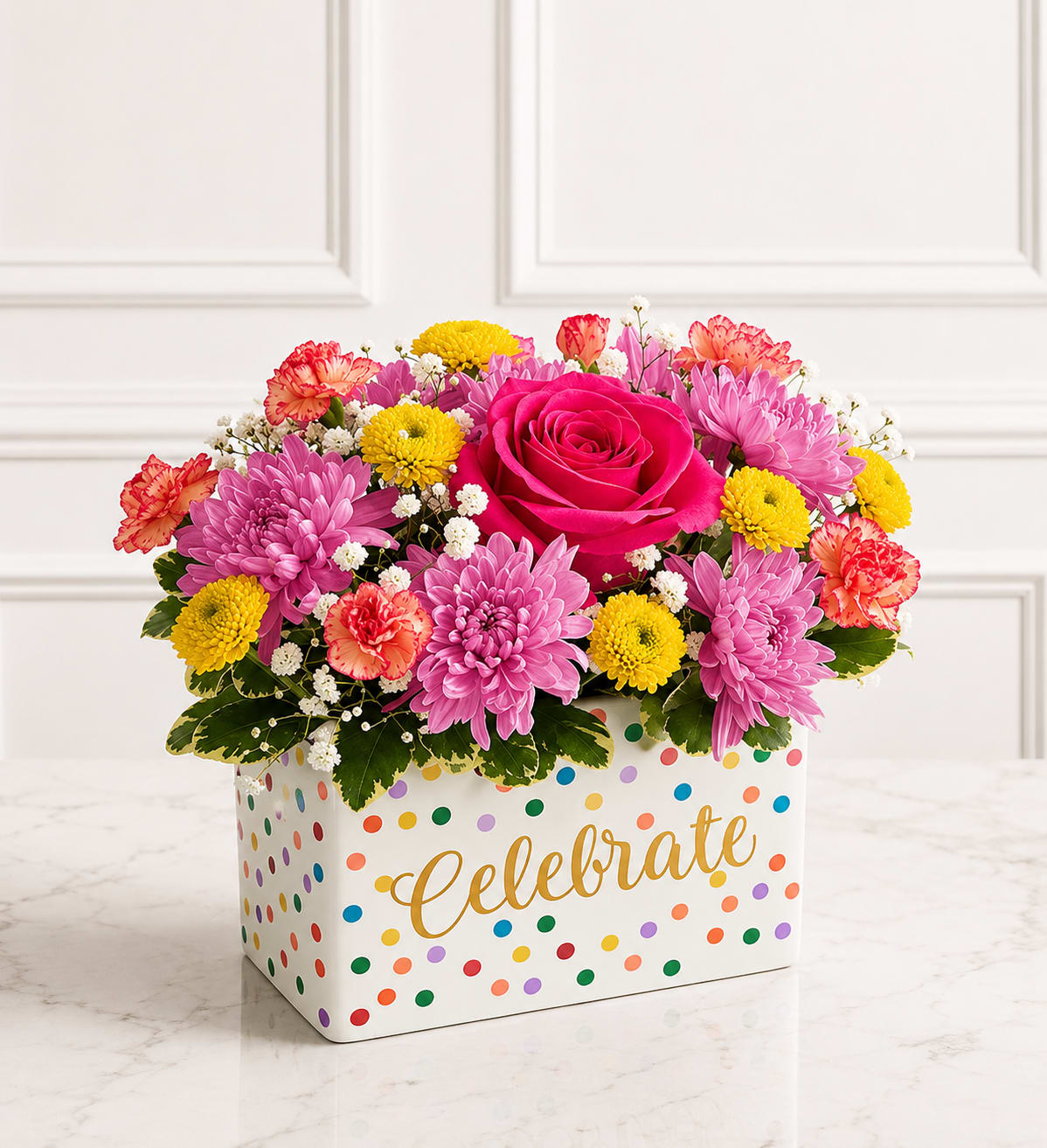 Celebrate With Joy™ - Celebrate every special moment with Celebrate With Joy™, a cheerful floral arrangement designed in a festive keepsake container. Featuring a vibrant hot pink rose, soft lavender cushion mums, pink mini carnations, sunny yellow button poms, delicate baby's breath, and fresh seasonal greenery, this colorful design is perfect for birthdays, congratulations, graduations, new jobs, or any occasion worth celebrating. A thoughtful gift that brings smiles long after the celebration begins.