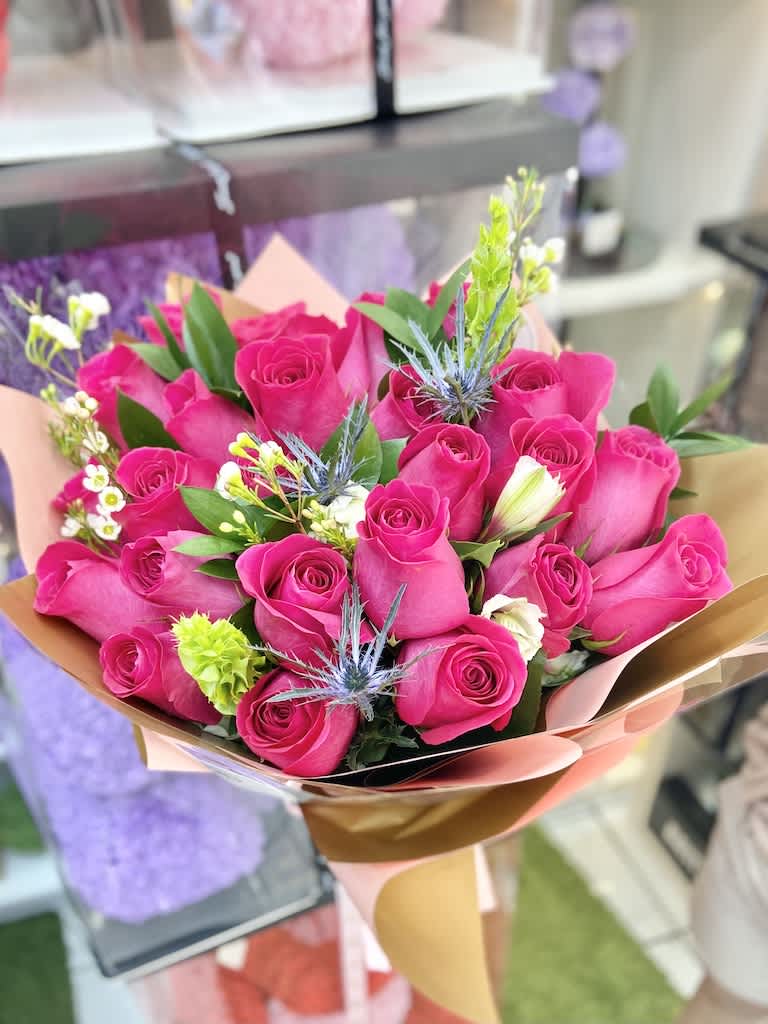 Hand-tied bouquet of bright pink roses with small white blooms and blue thistles wrapped in pink and gold paper