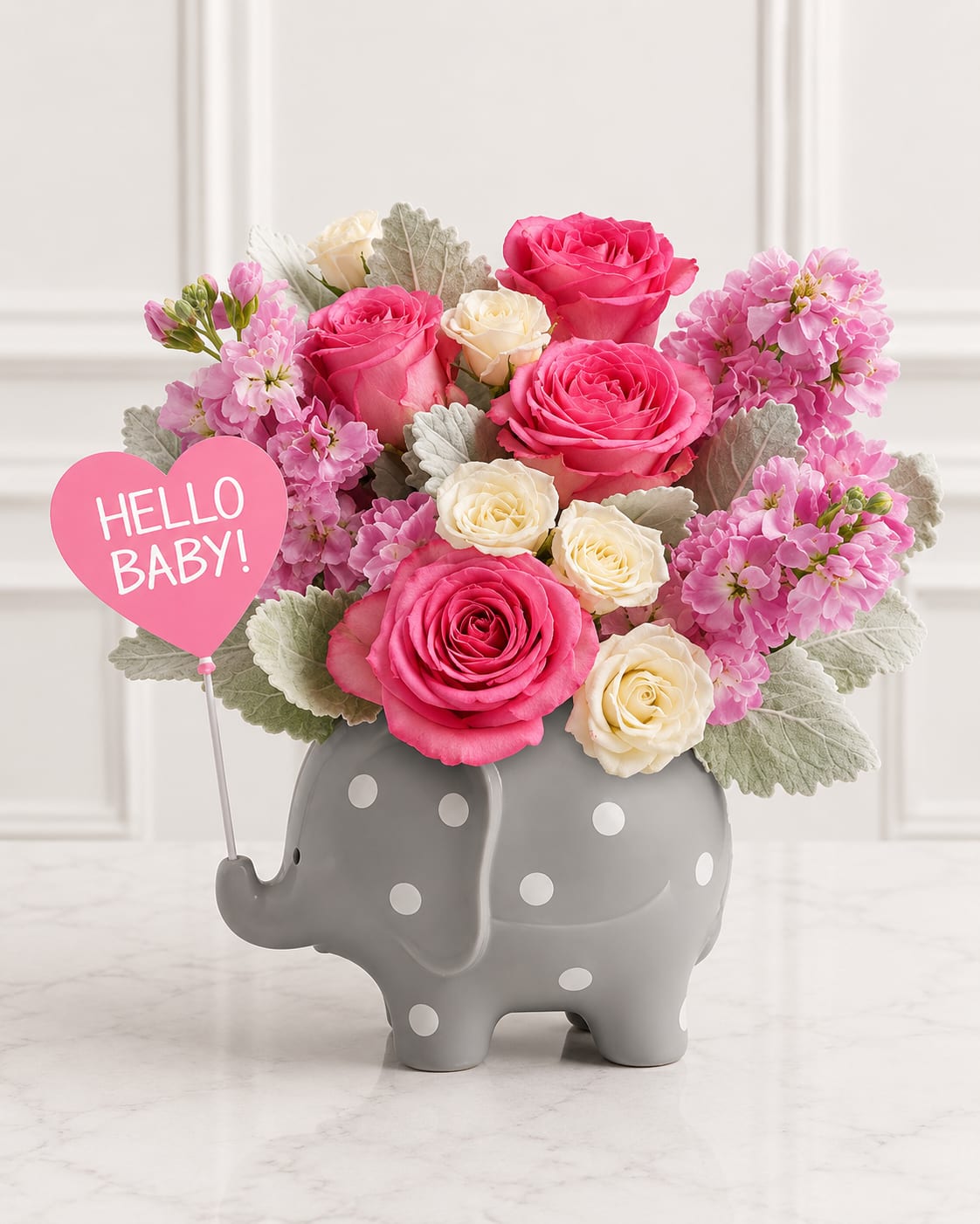 Hello Sweet Baby Girl™ - Welcome the newest little blessing with Hello Sweet Baby Girl™, a heartwarming arrangement featuring vibrant pink roses, delicate white spray roses, soft pink stock, fresh dusty miller foliage, and lush seasonal greenery. Designed in an adorable gray ceramic elephant keepsake with a charming "Hello Baby!" balloon pick, this sweet arrangement is the perfect gift to celebrate the arrival of a baby girl, a baby shower, or to congratulate proud new parents. The keepsake elephant planter can be treasured long after the flowers have bloomed.