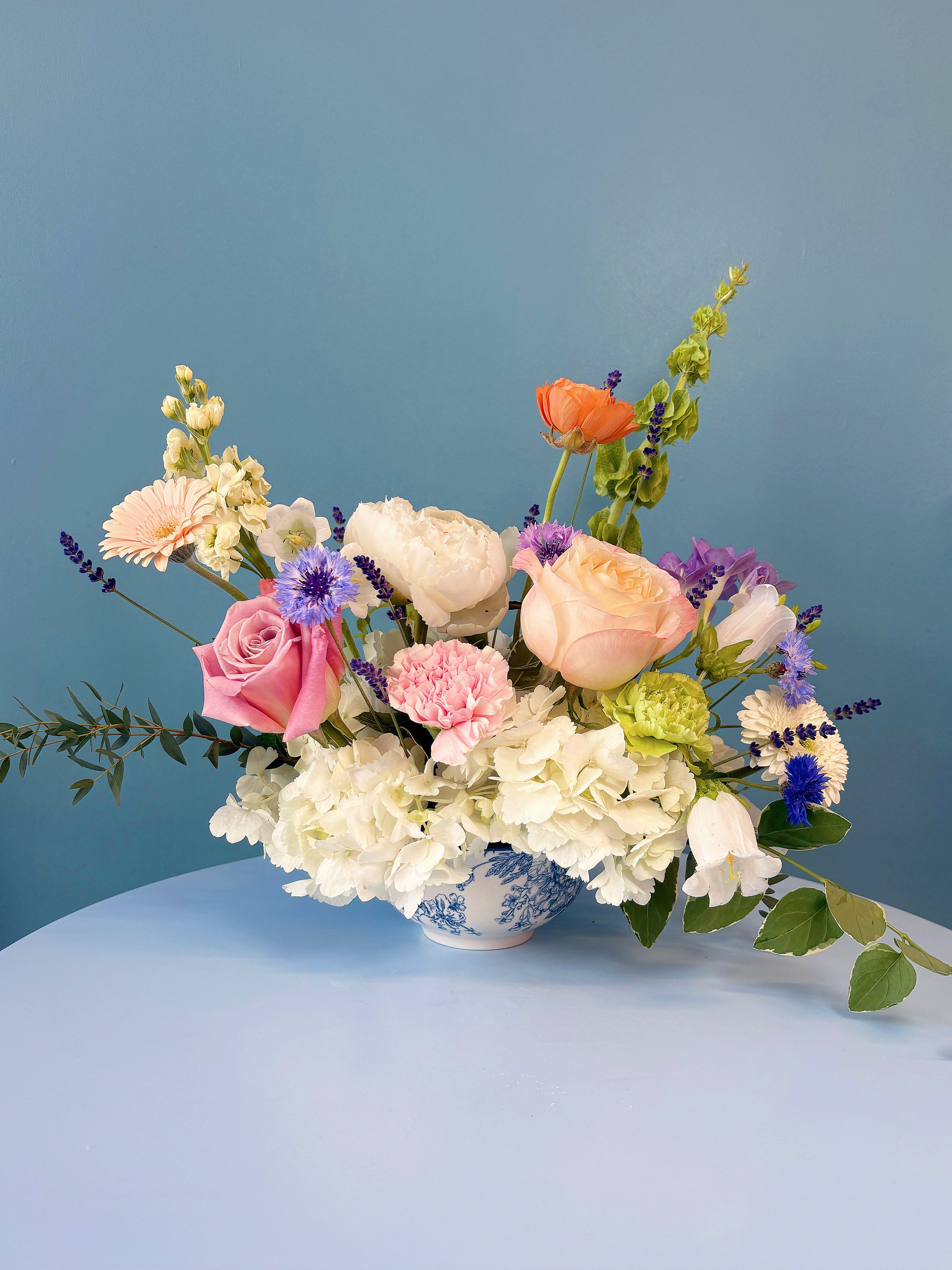Summer Victorian Garden table arrangement - Bring the timeless charm of an English garden into your home with our Summer Victorian Garden Table Arrangement, thoughtfully designed to capture the romance, elegance, and natural beauty of the season. Featuring a curated selection of premium seasonal blooms in soft, graceful hues, this garden-inspired design blends luxurious roses, delicate hydrangeas, peonies, cottage garden favorites, and whimsical textural florals with airy greenery. The result is an arrangement that feels effortlessly elegant, abundant, and full of movement. Presented in a classic blue and white porcelain inspired vessel, it makes a beautiful centerpiece for dining tables, garden parties, afternoon tea, bridal showers, or any occasion that calls for timeless sophistication. Romantic, fresh, and beautifully refined, this arrangement brings the charm of a blooming Victorian garden to every table while making a thoughtful gift for someone special.