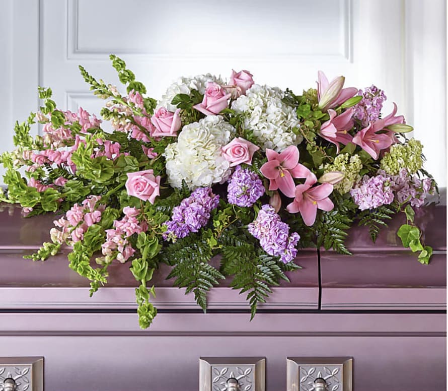 Pink lilies and roses arranged with white hydrangeas on a casket