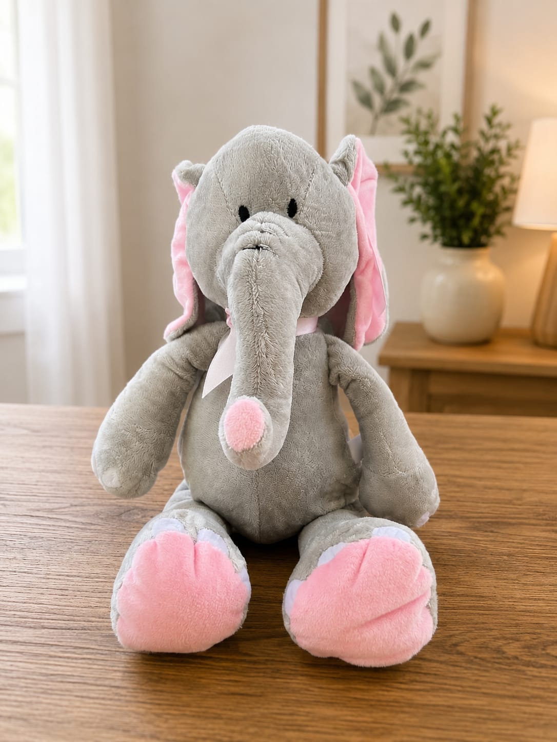 Blushing Cuddly Elephant - A cuddly gray plush elephant with soft pink accents makes this baby gift instantly irresistible-perfect as a baby shower bouquet alternative or a new-arrival present. The Blushing Cuddly Elephant pairs the plush's rounded, fuzzy texture and gentle pink-and-gray palette with a simple floral touch to send a warm, affectionate message: the kind of gift that makes a new parent or little one feel truly welcomed and loved.  The stuffed elephant features a soft gray body with pink on the ears, trunk tip, and feet, seated upright for an instant snuggle-ready display. Sized to sit beside a crib or on a nursery shelf, it complements pale pink, white, or neutral floral stems and works well as a standalone keepsake or an add-on to a small arrangement. Ideal for baby showers, newborn visits, or a thoughtful "just because" present, care is simple-spot clean the plush as needed and enjoy a lasting cuddly reminder of your congratulations.