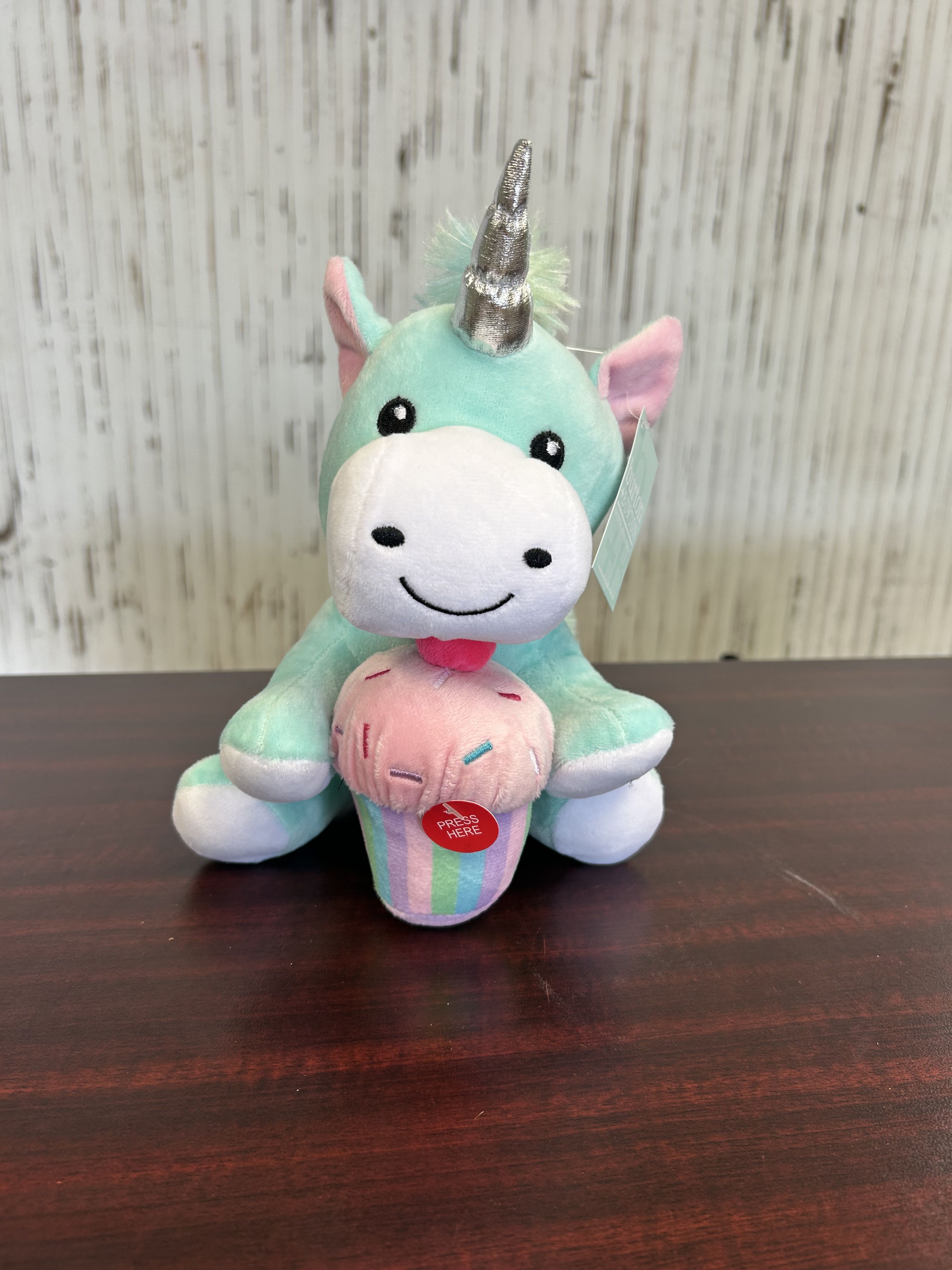 Magical Musical Unicorn - A pastel mint-blue plush unicorn with a shiny silver horn and pink ears greets the recipient-perfect as a birthday bouquet companion or a cheerful children's gift. This playful gift set works for birthdays, congratulations, or anytime you want to make a child (or the young at heart) feel delighted; the included press-button sound makes the moment memorable and joyful.  The small seated unicorn holds a pastel-striped ice cream cone plush and features a white muzzle and a red "press here" sound button on the front; a hang tag adds a ready-to-gift touch. Colors include soft blues, pinks, whites, and a touch of purple in the palette, making it easy to pair with seasonal flowers or a mixed pastel arrangement if you'd like to add blooms for extra sparkle.  Sized as a compact keepsake, this whimsical plush is designed to be cuddled and displayed-she'll feel noticed and celebrated every time she presses the button. Order as a standalone children's surprise or combine with a small bouquet for a complete birthday or celebratory presentation.