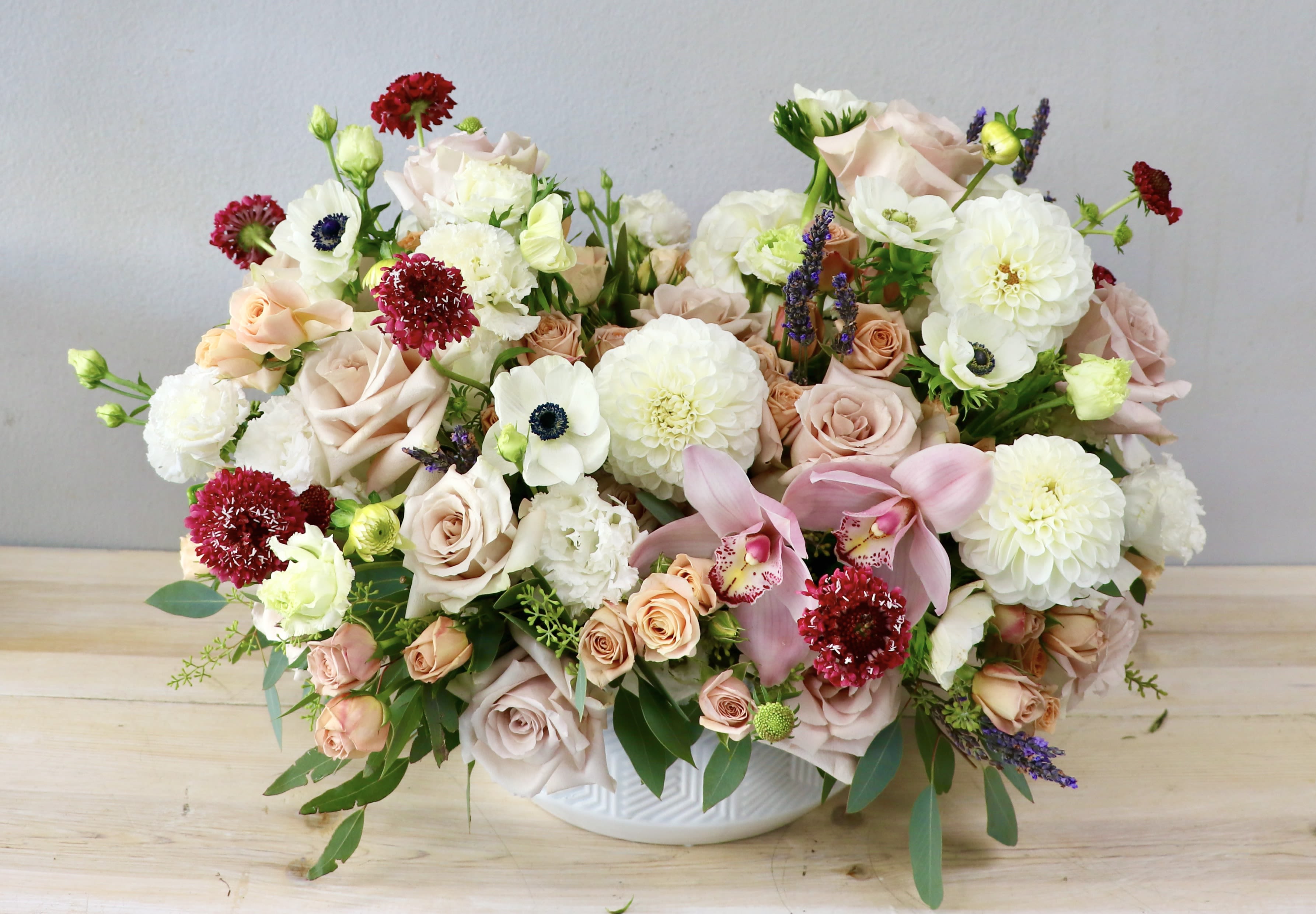 Mixed bouquet of blush roses, white blooms, and pink orchids in a white bowl vase