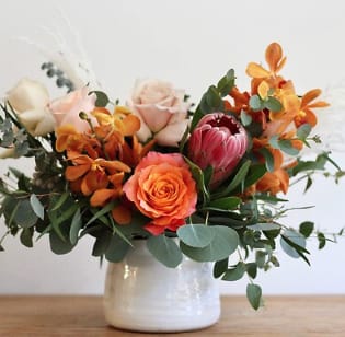 Low arrangement of orange and blush flowers in a white ceramic pot