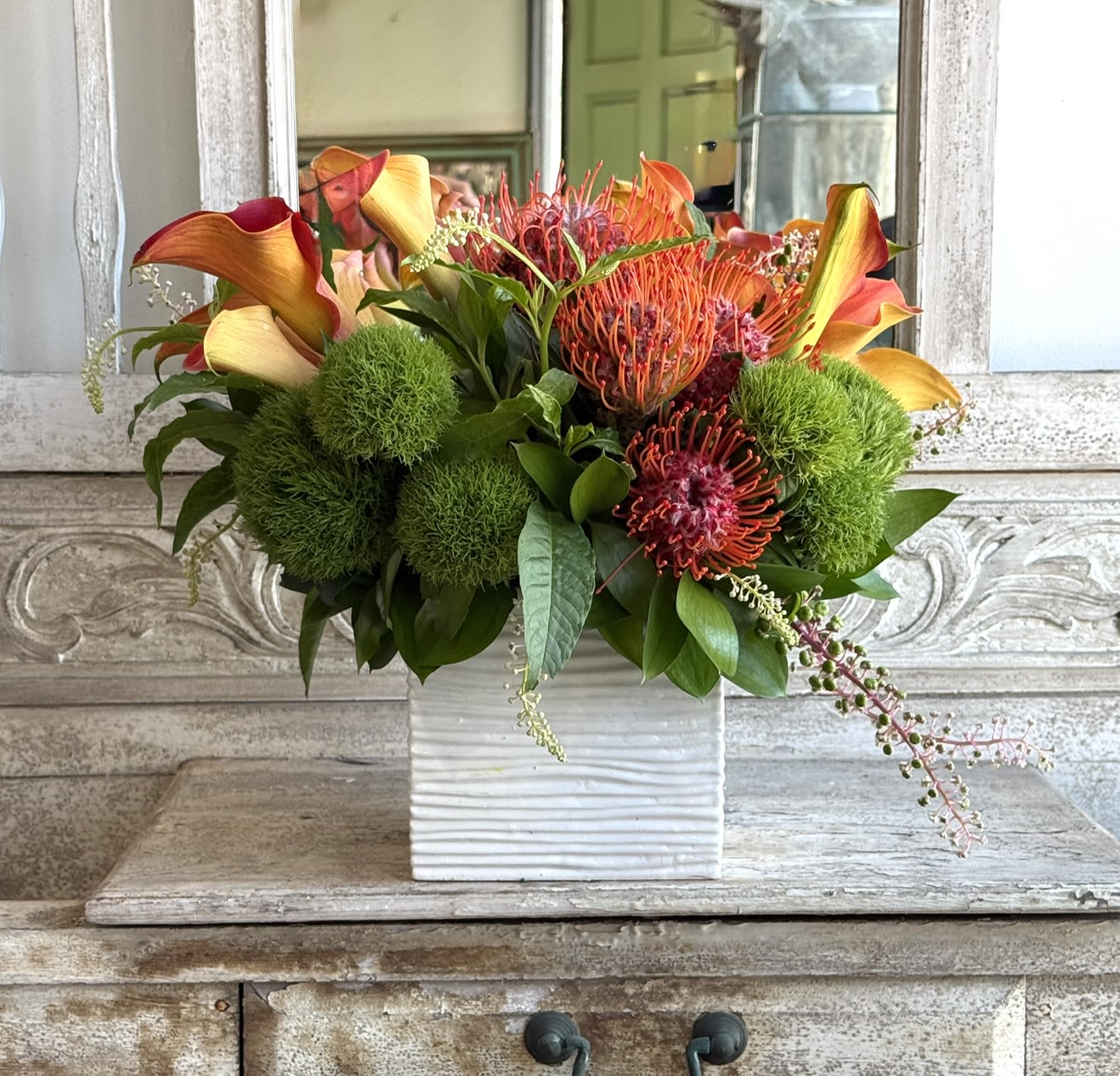 Orlando  - Orange and yellow calla lilies with pink-orange pincushions, Protea and bright green ball Dianthus in a white square ceramic vase-vibrant, tropical and cheerful for everyday display.