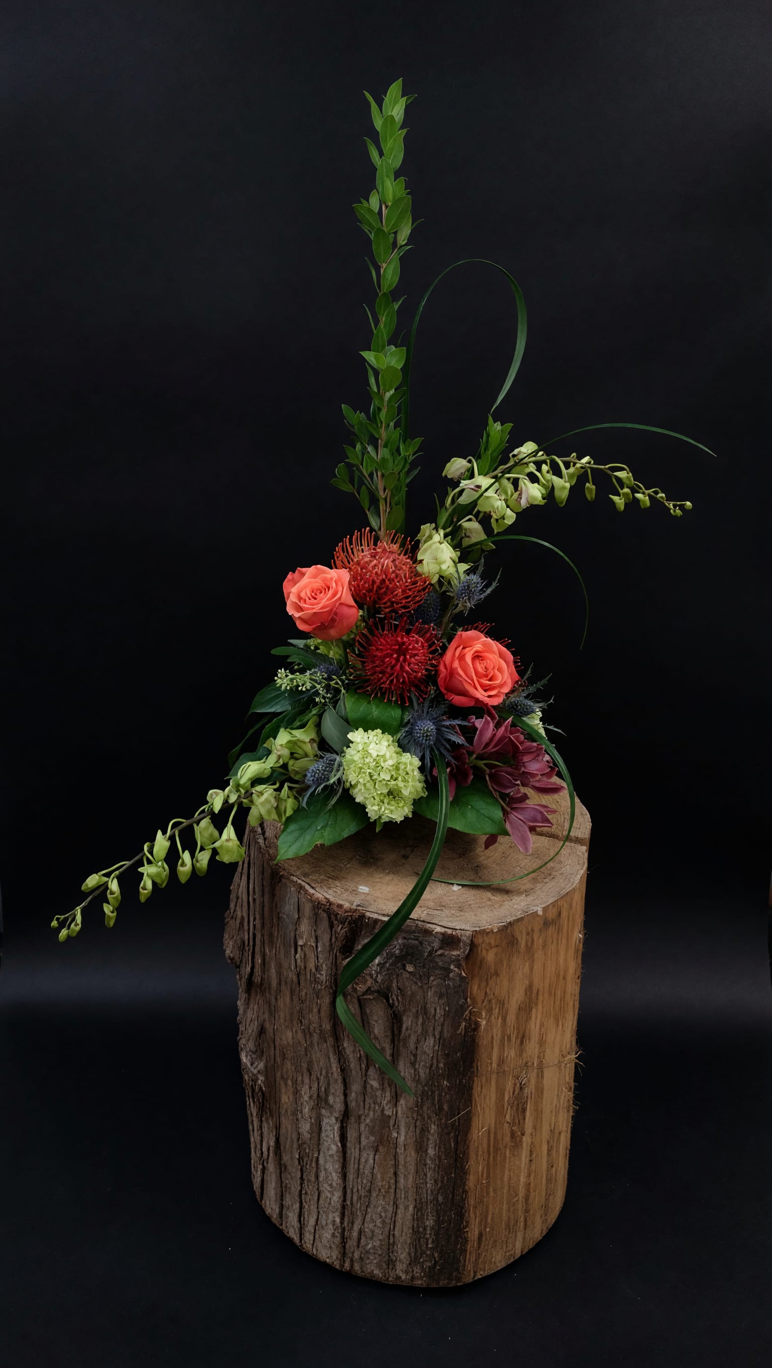 Woodland Blush Floral Arrangement - A rustic and romantic floral design featuring soft blush roses, rich burgundy blooms, creamy white accents, and fresh seasonal greenery. Artfully arranged on a natural wood base, this one-of-a-kind design brings warmth and elegance to birthdays, anniversaries, thank-you gifts, housewarmings, or any special occasion.