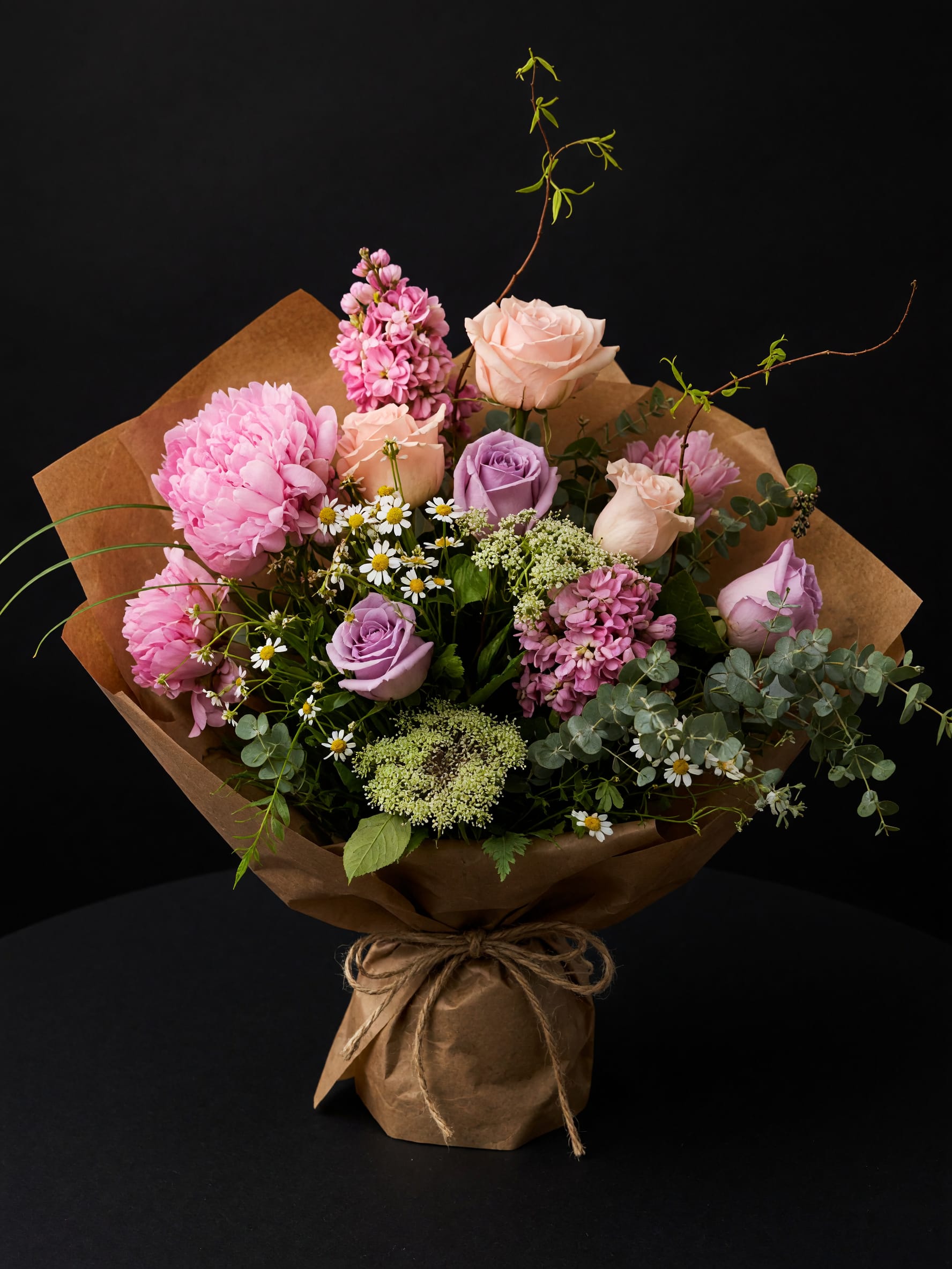 Bouquet of pink and lavender roses with mixed blooms in brown paper wrap