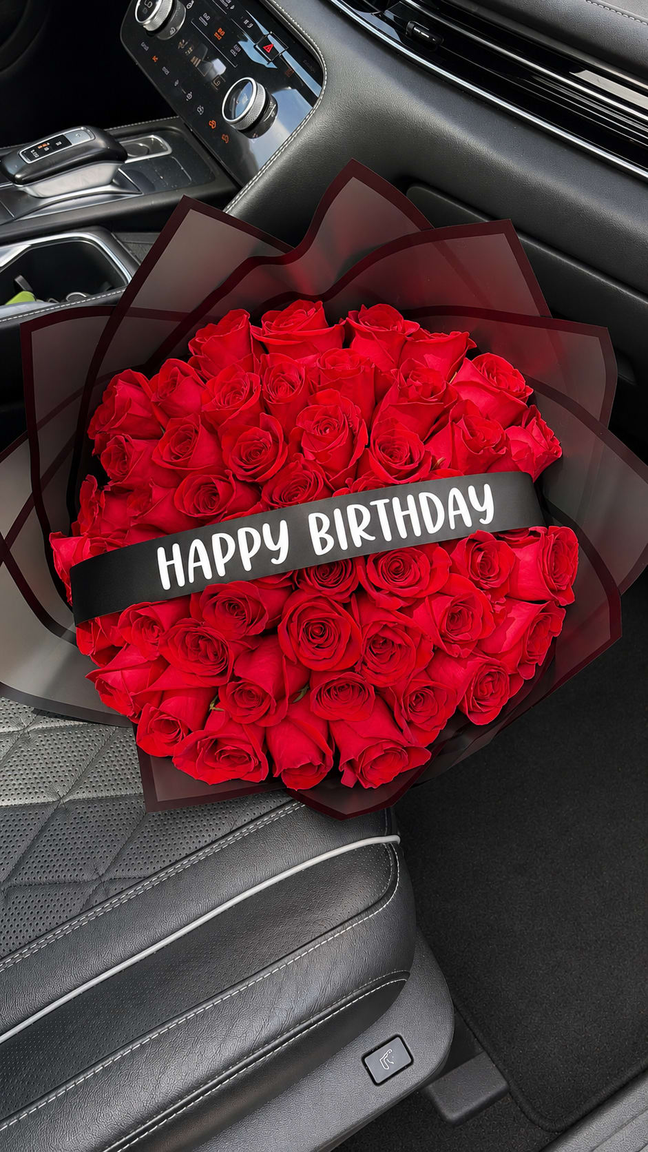Birthday Bouquet - A bold hand-held birthday bouquet that reads as both romantic and celebratory: deep red roses packed tightly and wrapped in dark translucent black paper create a striking red-and-black contrast that makes the recipient feel truly seen. The black birthday ribbon across the center plainly says "HAPPY BIRTHDAY," so she'll know this is a special, festive surprise the moment it arrives-perfect for anniversaries, milestone birthdays, or any romantic celebration.  This arrangement uses classic long-stem red roses arranged densely for visual impact and wrapped in sleek black wrapping paper for a modern, dramatic silhouette. The birthday ribbon is integrated across the center for immediate messaging; the bouquet is sized for hand delivery rather than vase display, making it an ideal gift to present at the door or bring to a party.  Give this to the person you want to make feel celebrated and adored-she'll feel the romance and the occasion at once. Order with standard delivery options; to keep the roses fresh, remove wrapping and place stems in water as soon as possible.