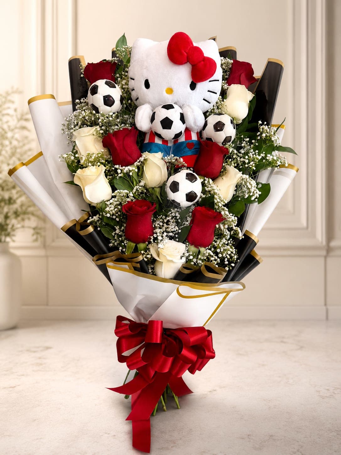 Hello Kitty MVP Bouquet  - Score big with a gift that’s as sweet as it is unforgettable! This playful bouquet features a lovable Hello Kitty plush surrounded by a beautiful mix of red and white roses, delicate baby’s breath, fresh greenery, and fun soccer accents. Wrapped in elegant black and white paper with gold details and finished with a bold red bow, this design is perfect for soccer fans, birthdays, graduations, celebrations, or anyone who loves Hello Kitty.