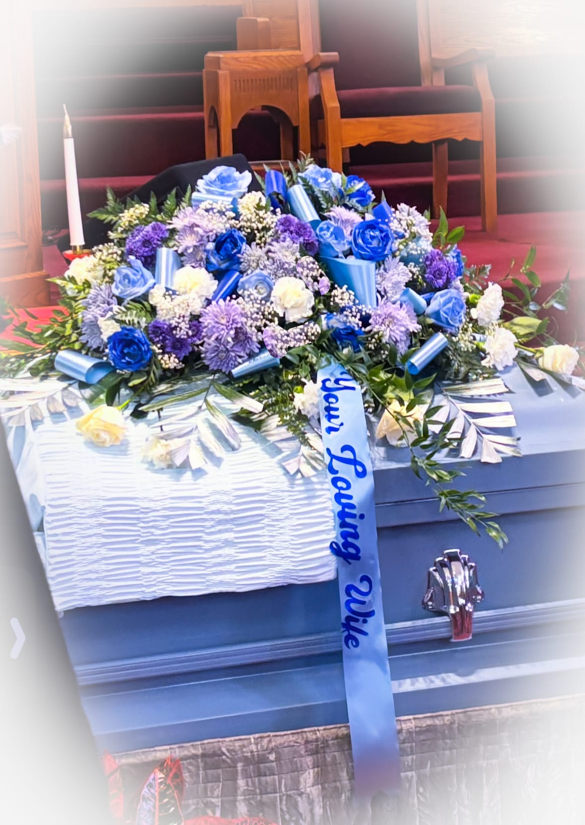 Blue and white floral casket spray with ribbon on a coffin
