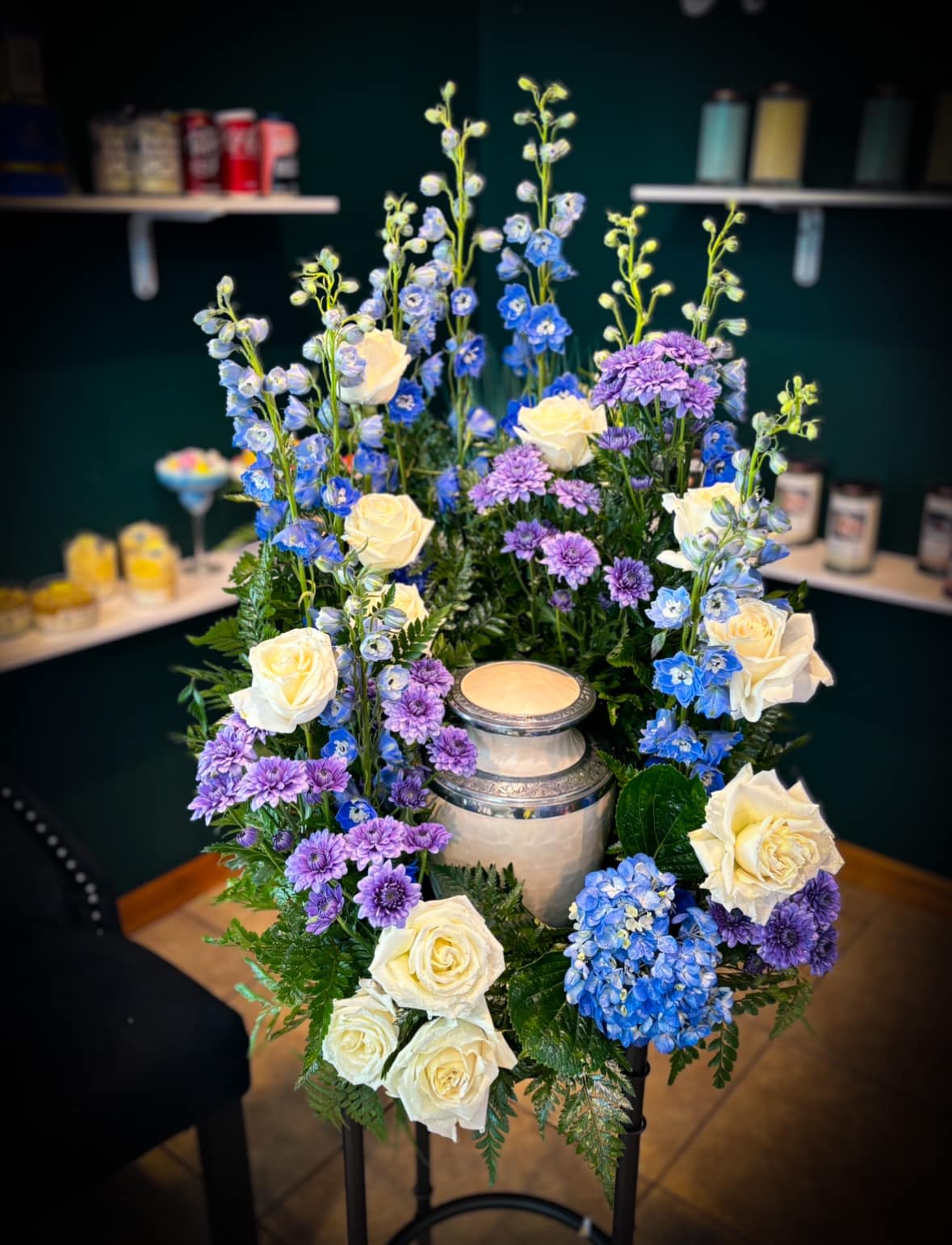 Tall floral arrangement with white roses, blue delphinium, and purple mums around a candle