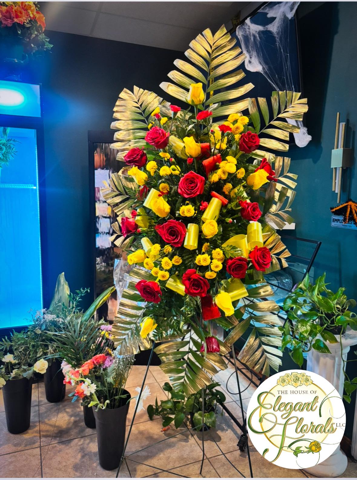 Tall floral standing spray with red and yellow roses and palm fronds