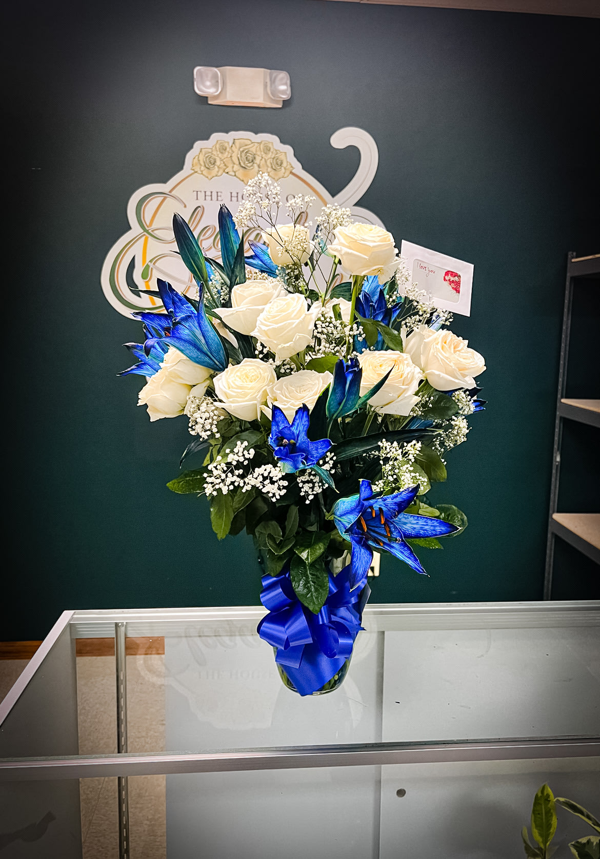 White roses and blue lilies in a glass vase with a blue ribbon