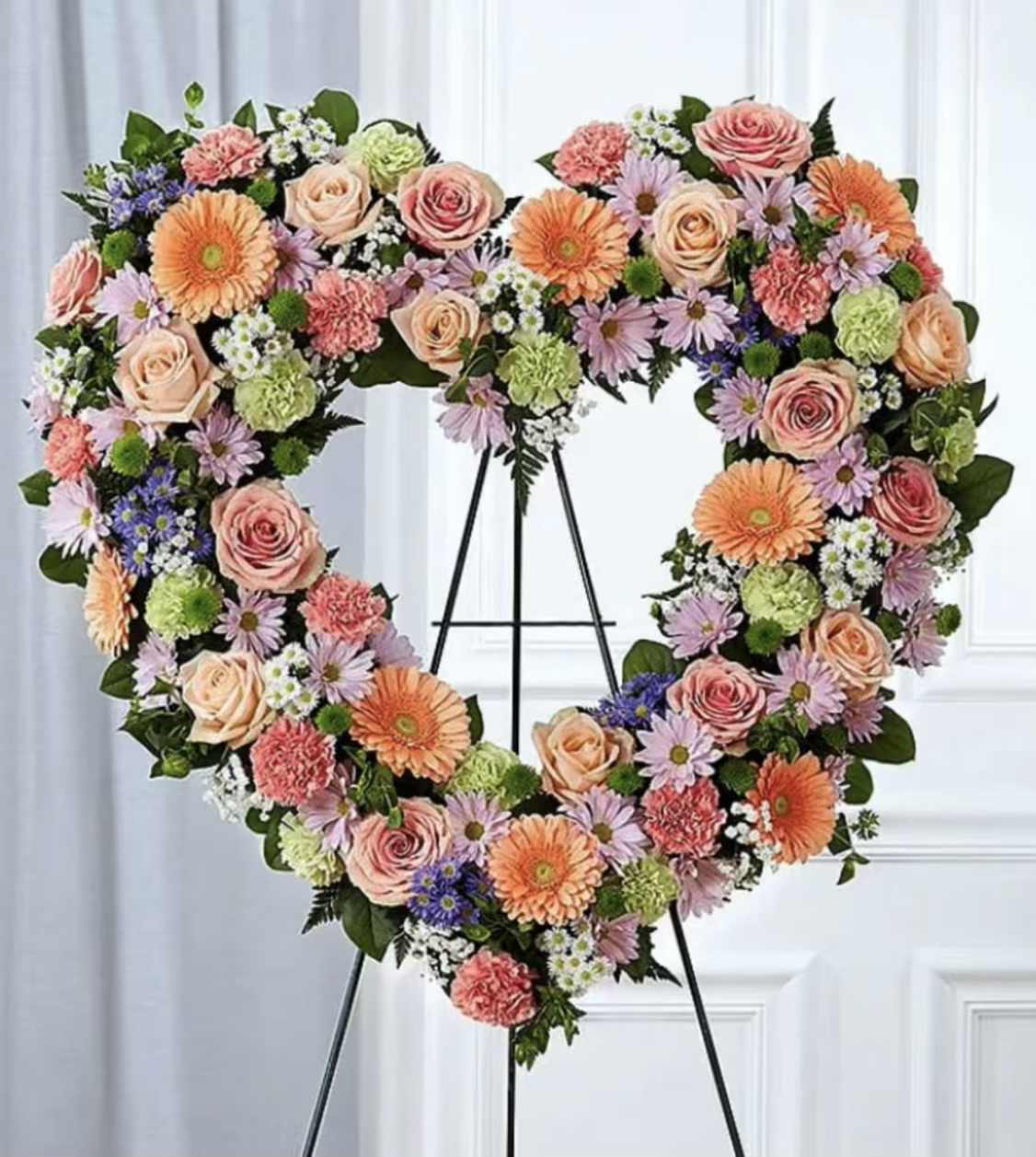 Heart-shaped floral wreath on a black stand with pink, peach, and purple flowers