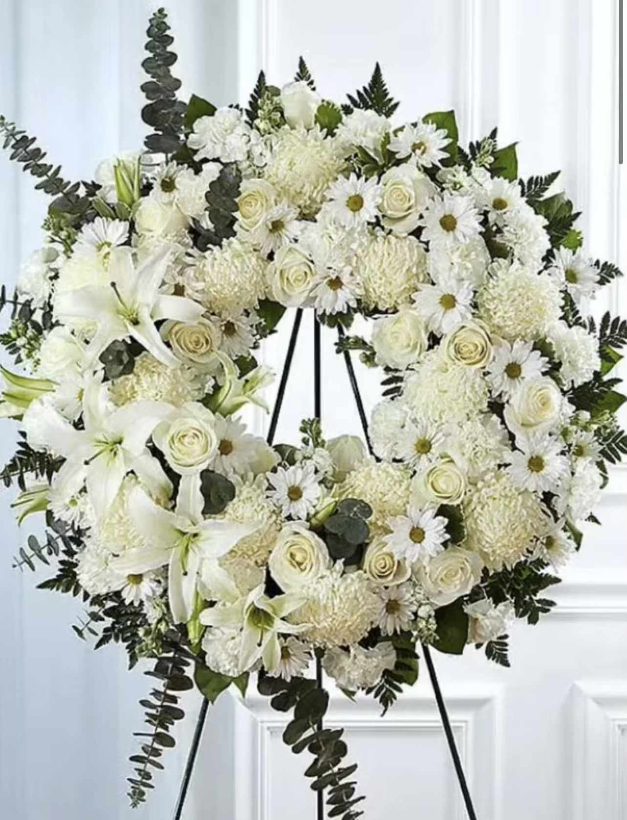 White floral wreath on a black easel with lilies and roses
