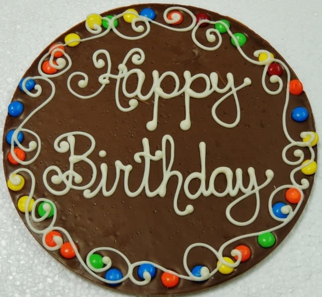 Round chocolate birthday cake with white icing and colorful candy border