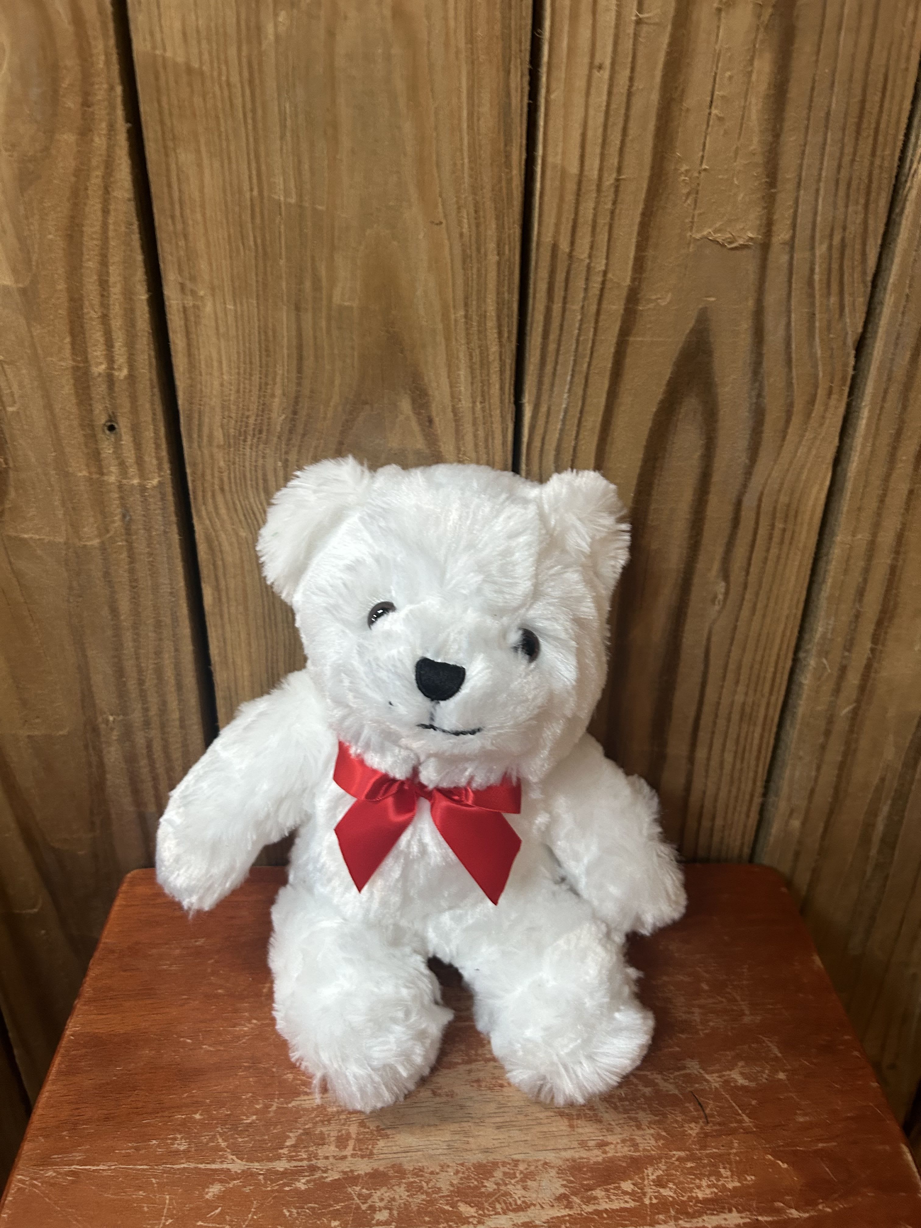 Small white teddy bear with a red bow sitting on a wooden surface.